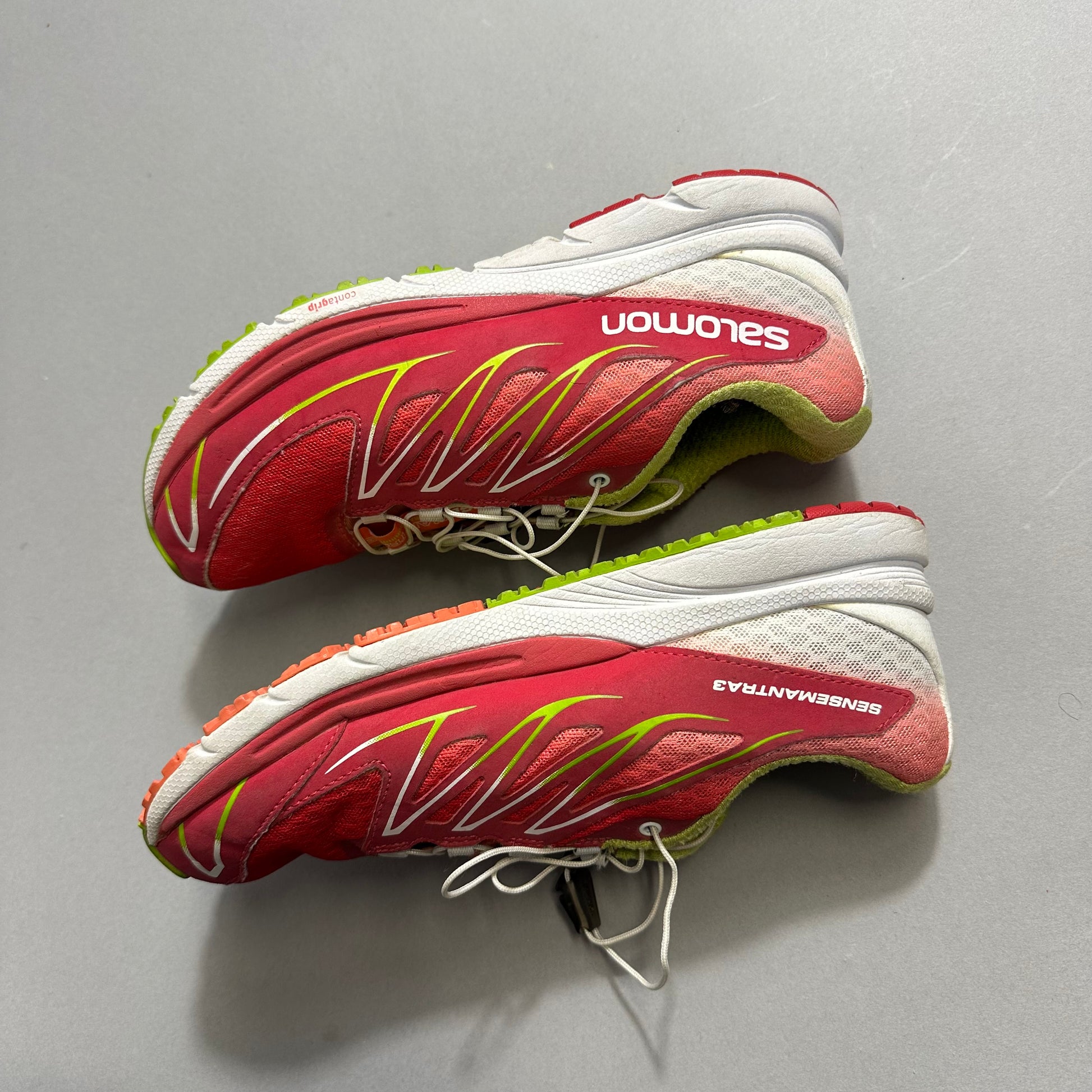 Red and white Salomon running shoes on a gray surface.