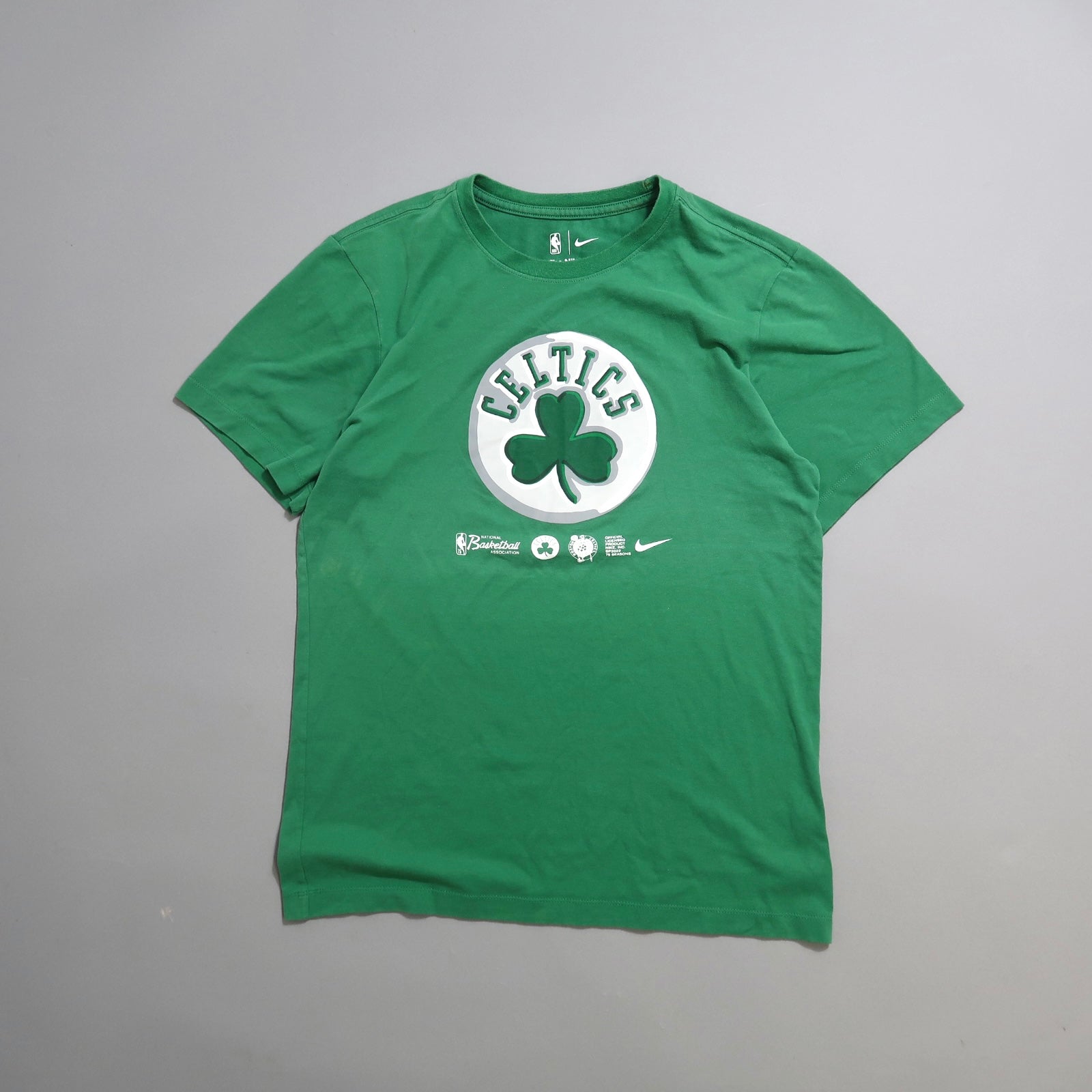 Green Celtics T-shirt with shamrock logo on a gray background.