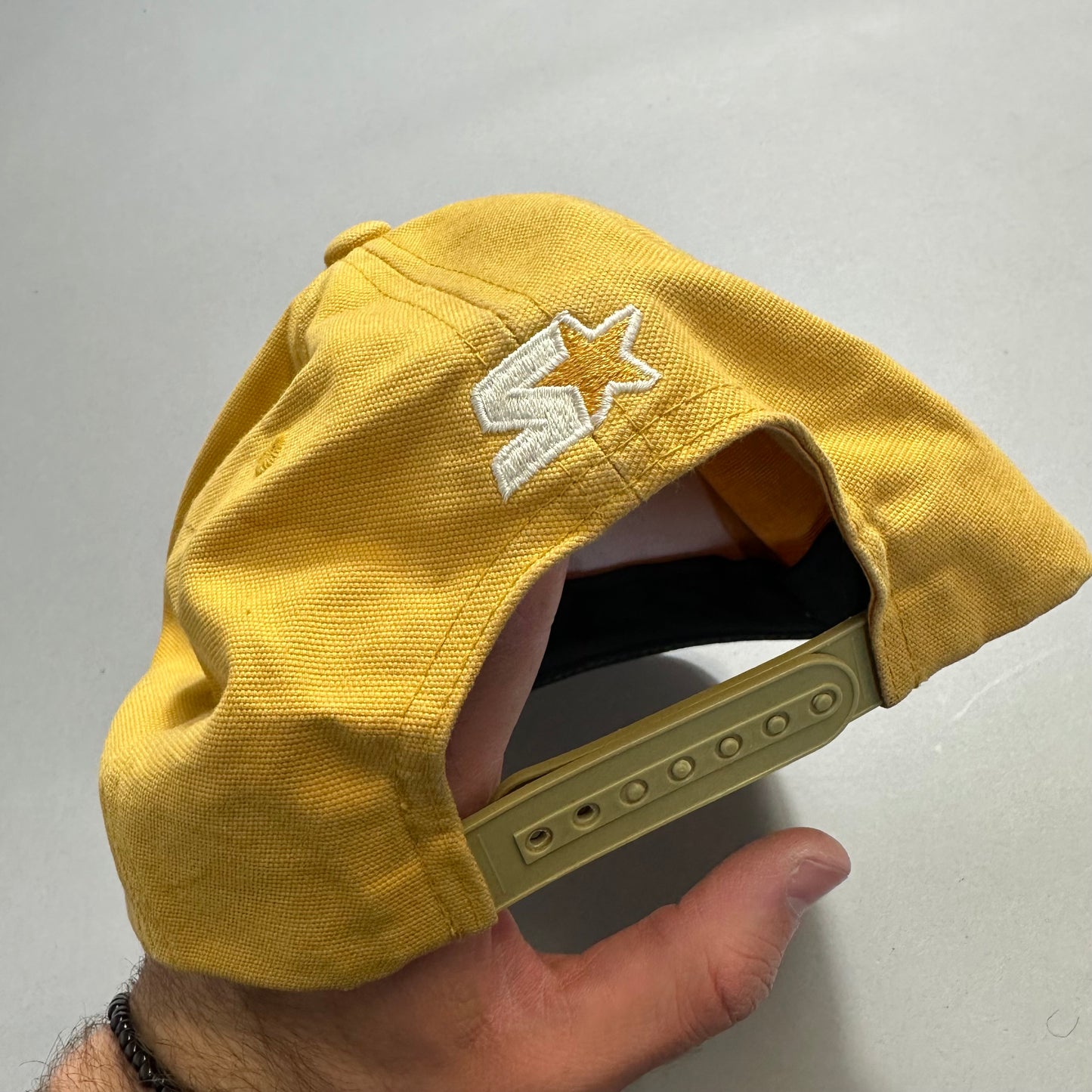 Yellow cap with star logo, adjustable strap held by hand.