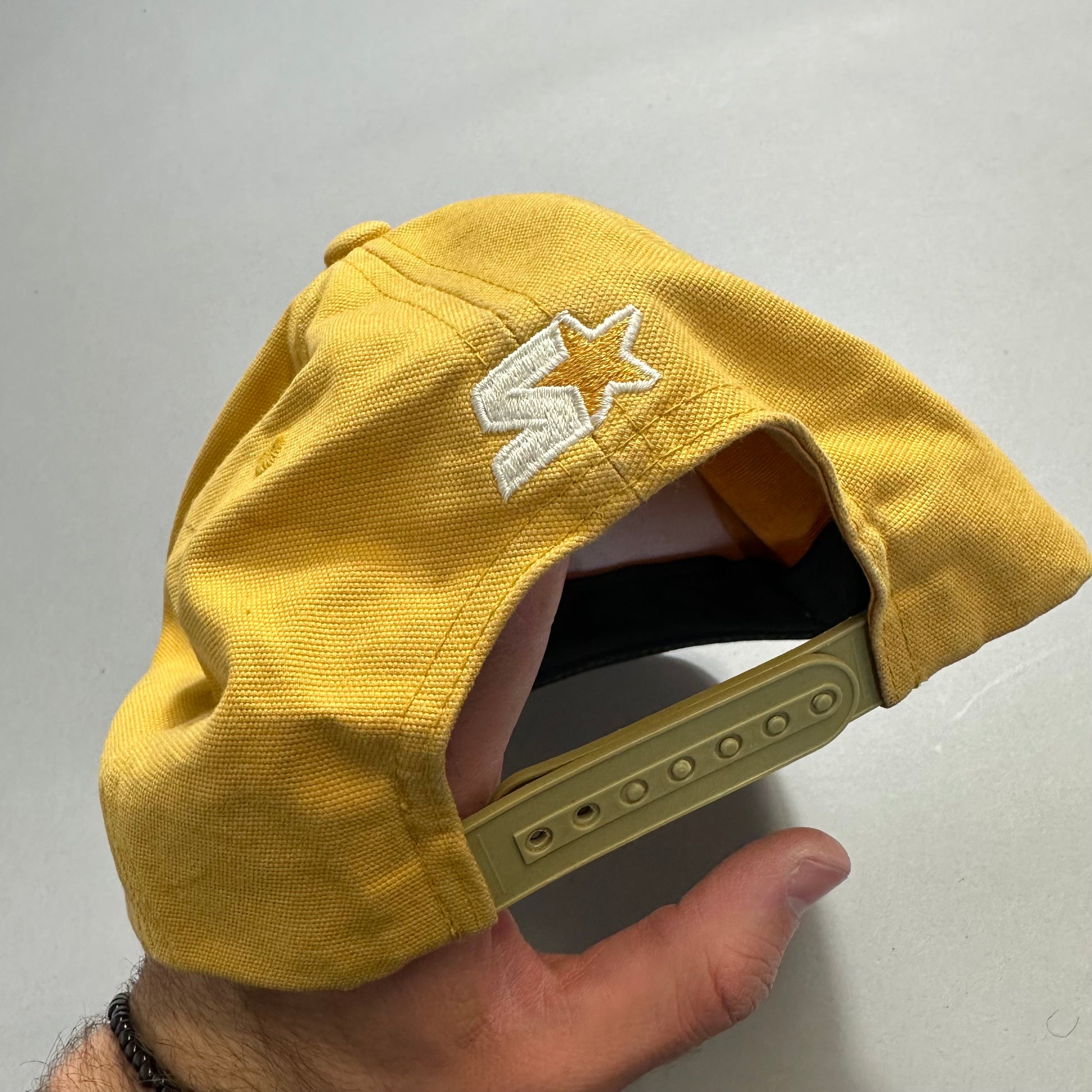 Yellow cap with star logo, adjustable strap held by hand.