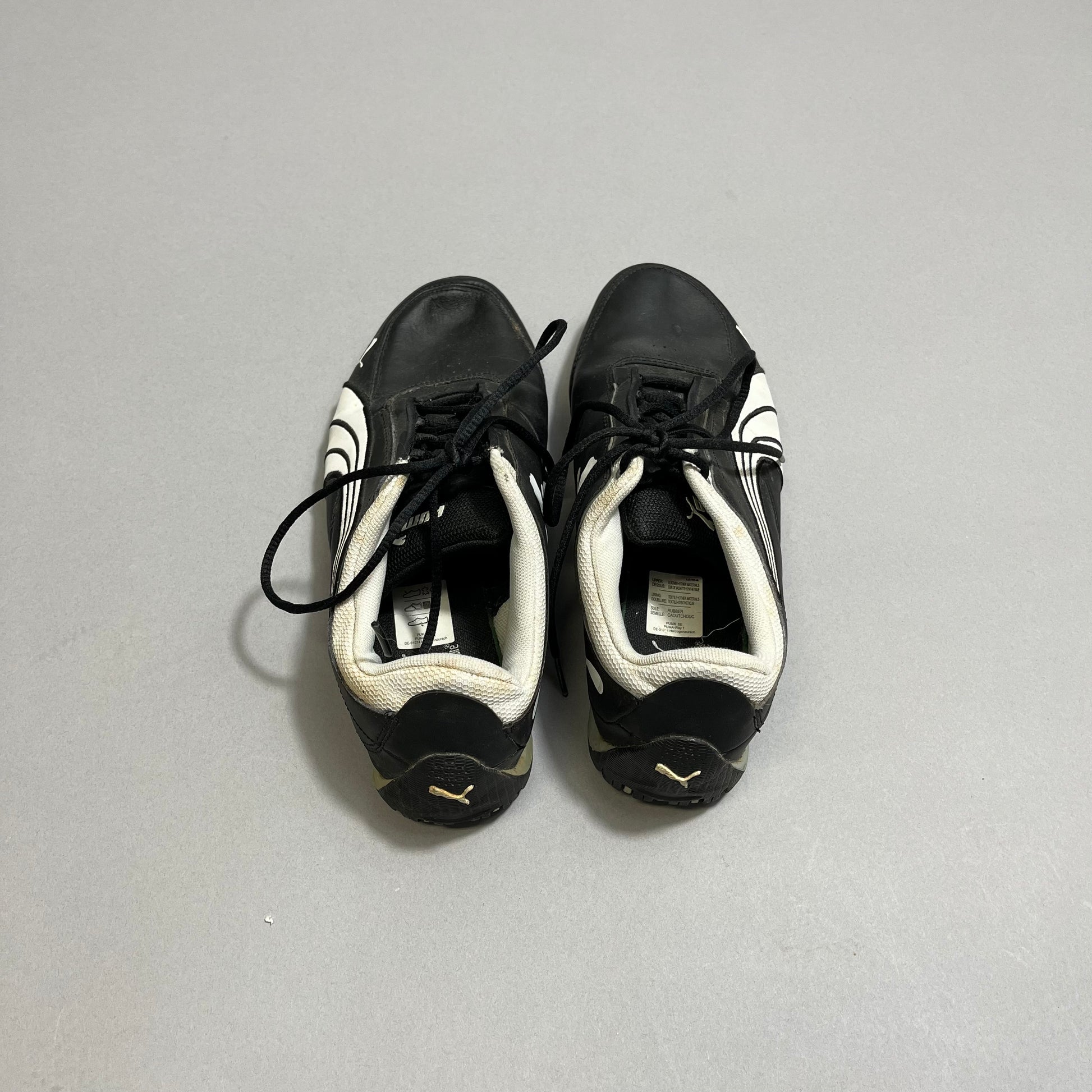 Black and white athletic shoes with laces on a gray surface.