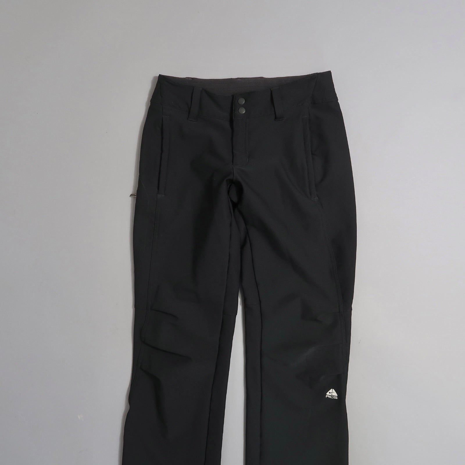Black pants with front pockets and buttons, displayed on a flat surface.