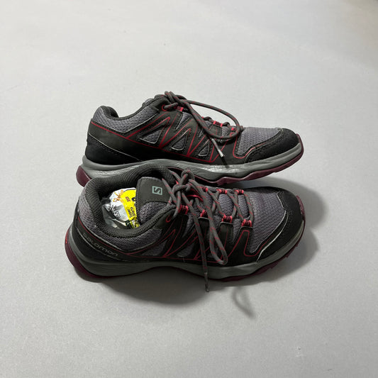 Gray and red trail shoes on a gray surface, one filled with paper.