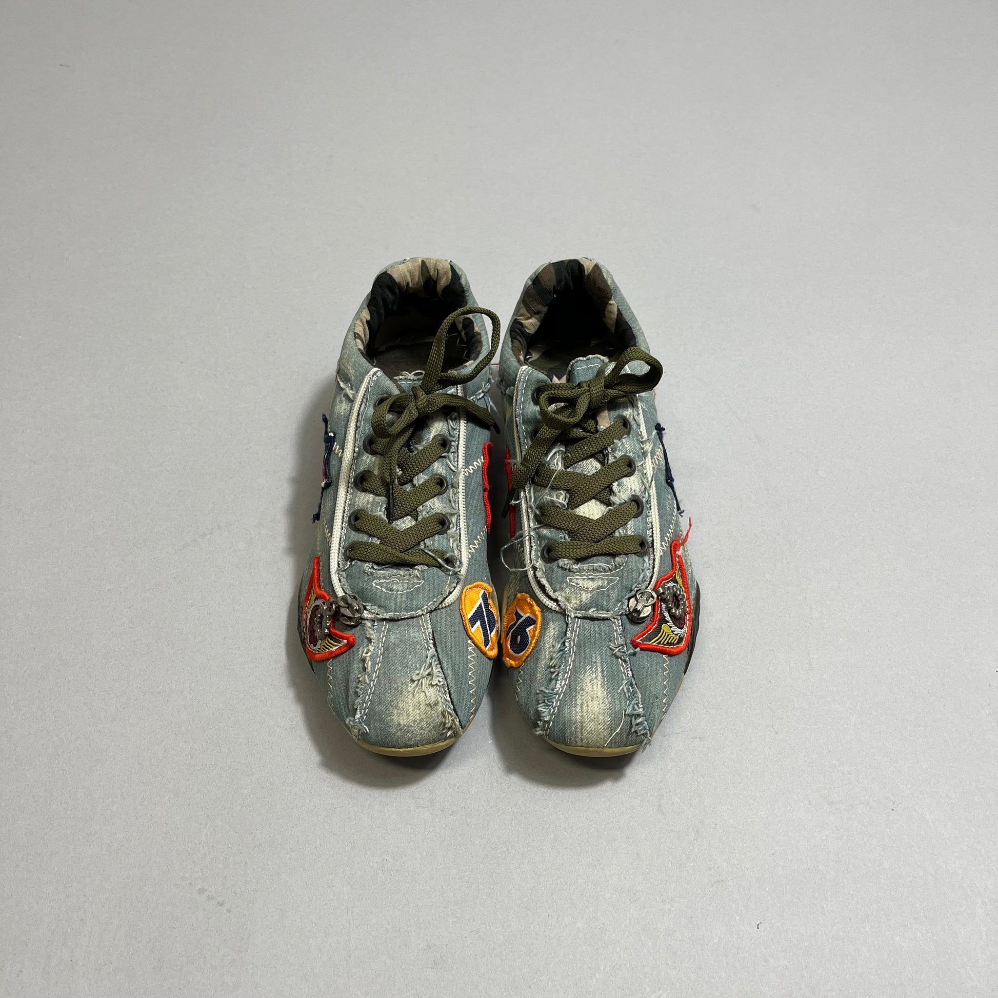 Distressed denim sneakers with colorful patches and green laces.