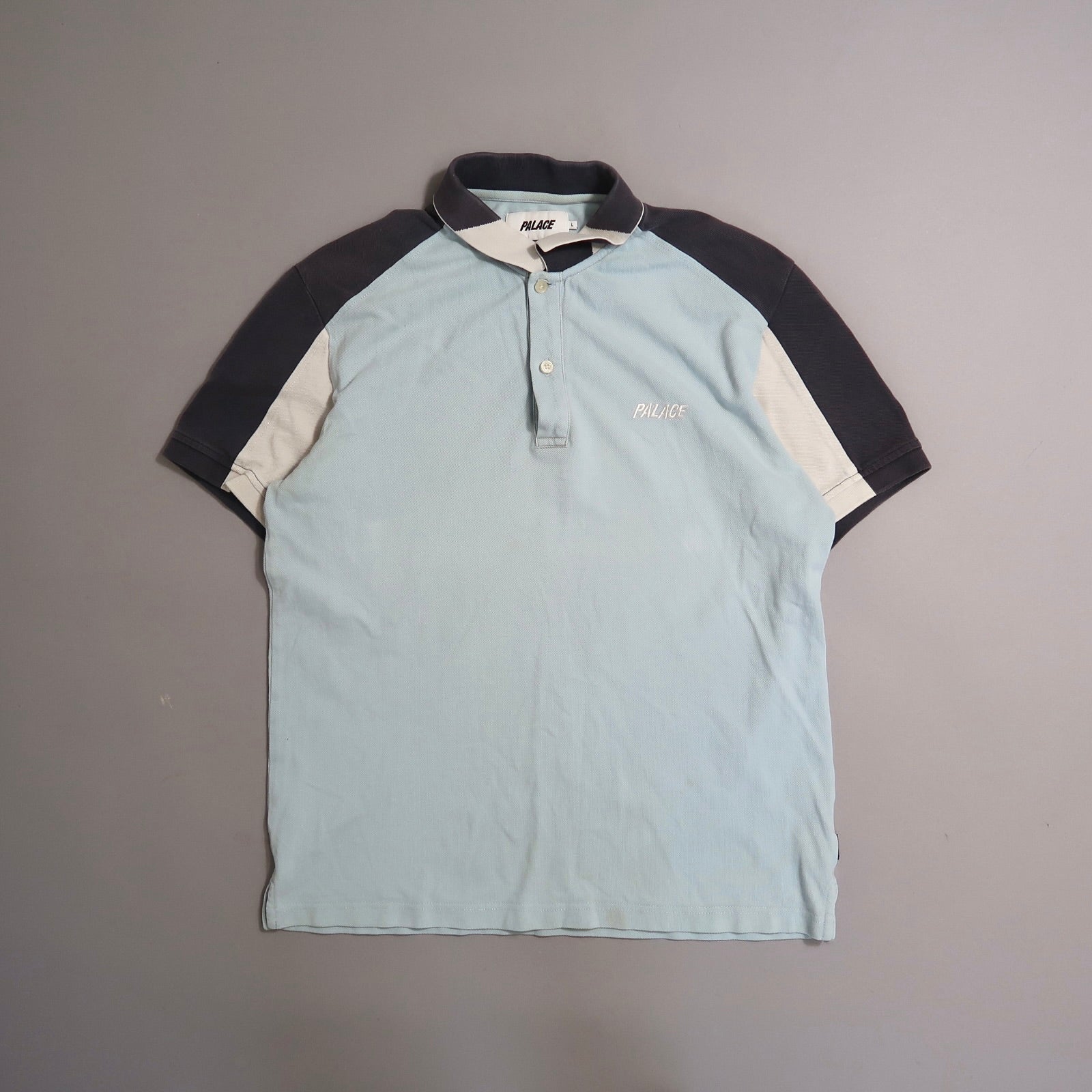 Light blue and black polo shirt with nullPalacenull text on chest.