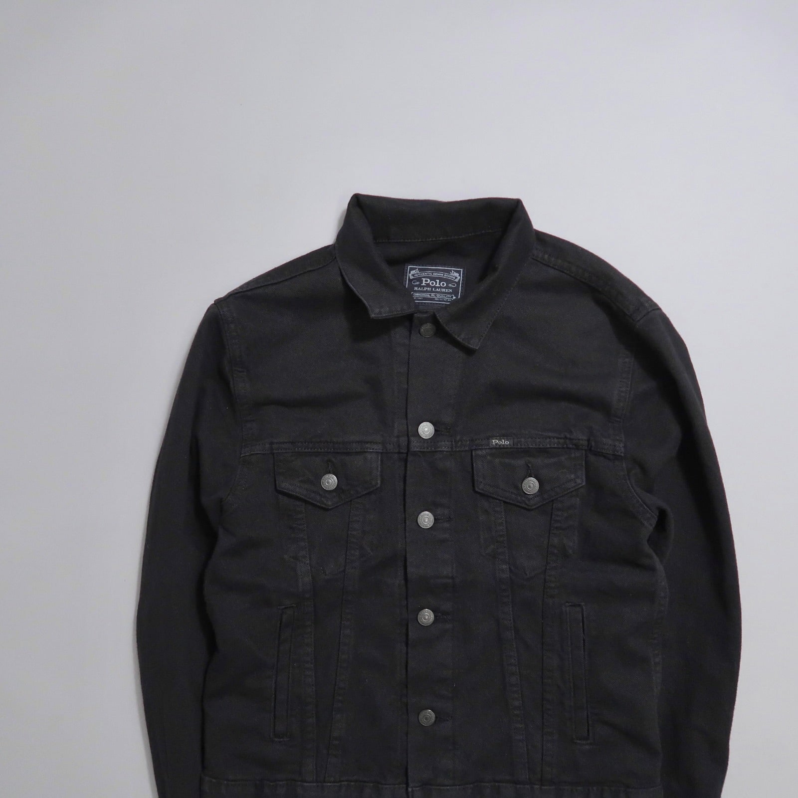 Black denim jacket with button details, laid flat.