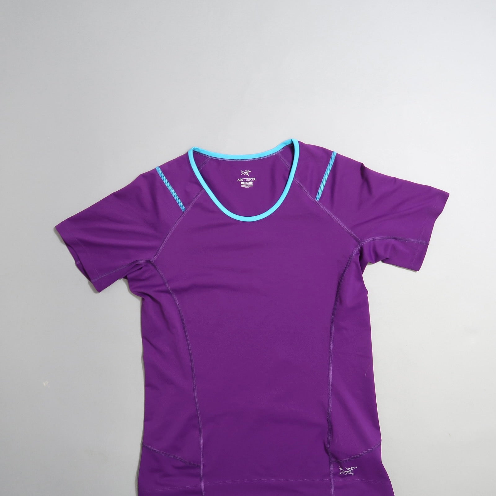 Purple athletic t-shirt with light blue neckline on a flat surface.