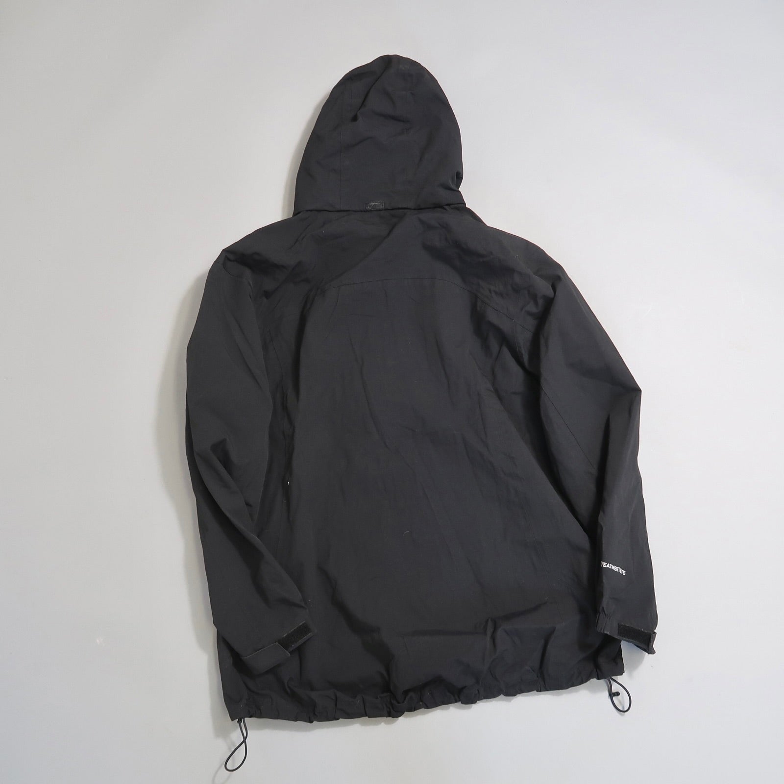 Black hooded jacket viewed from the back on a plain background.