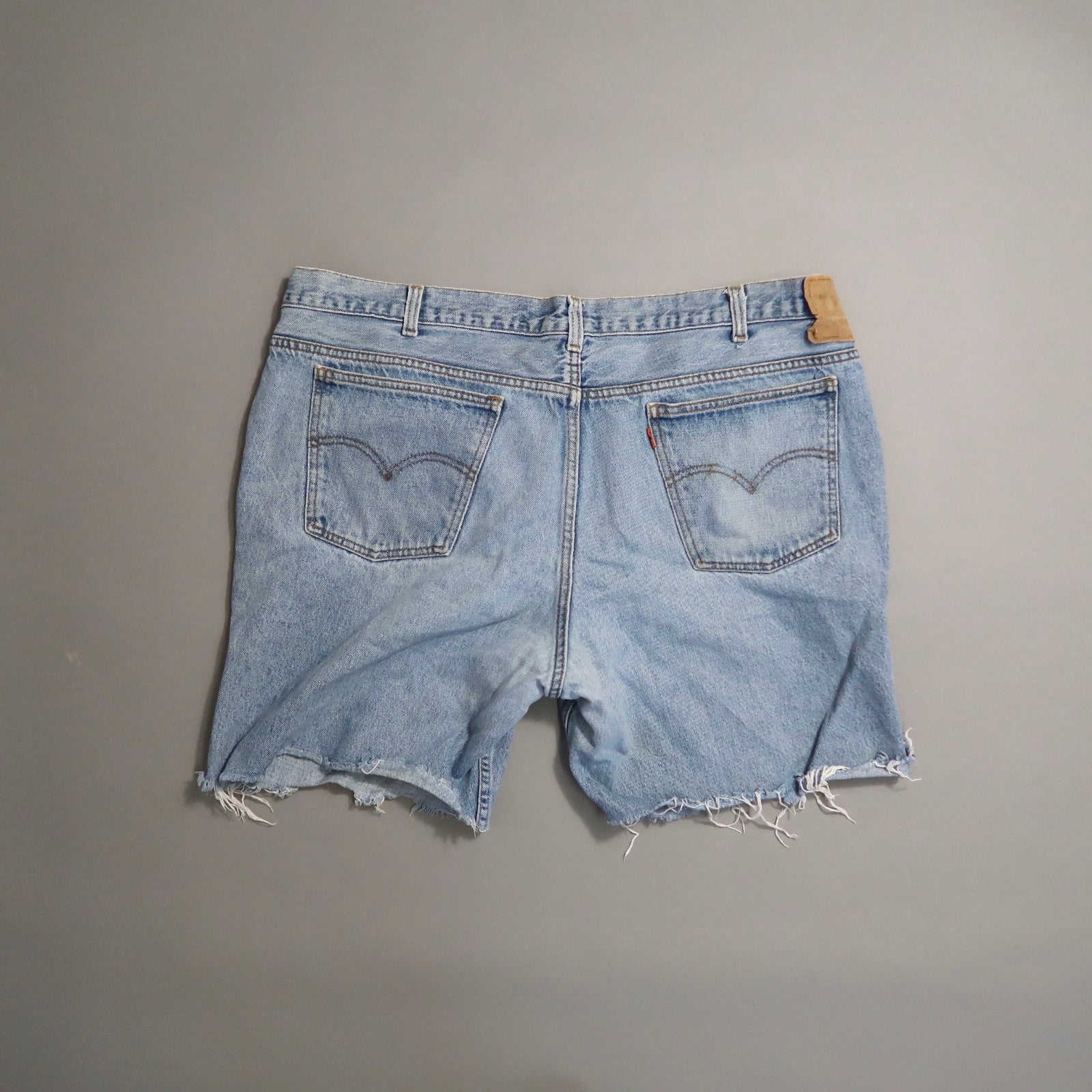 Frayed edge denim shorts with back pockets on a neutral background.