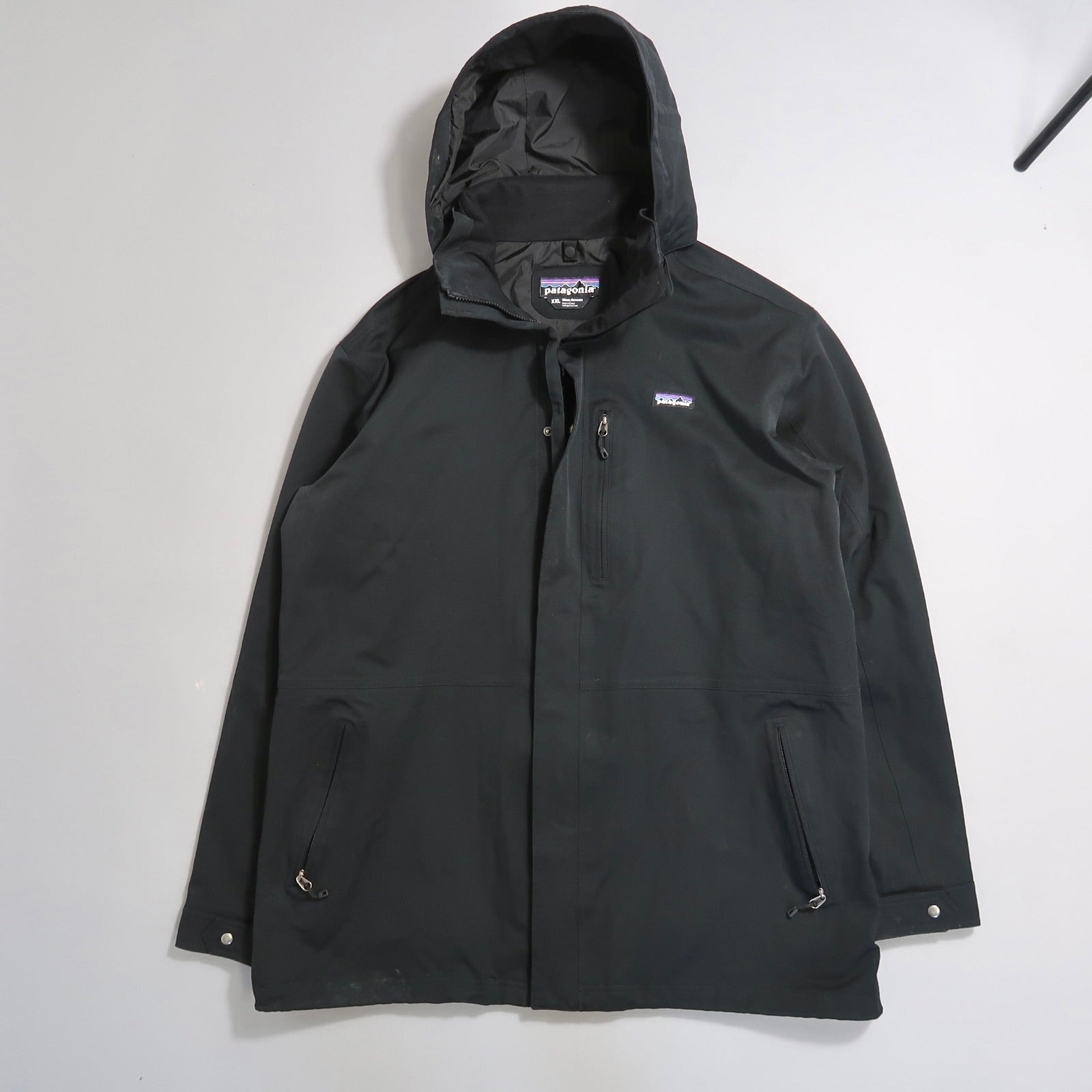 Black hooded jacket with front zipper and pockets on a flat surface.