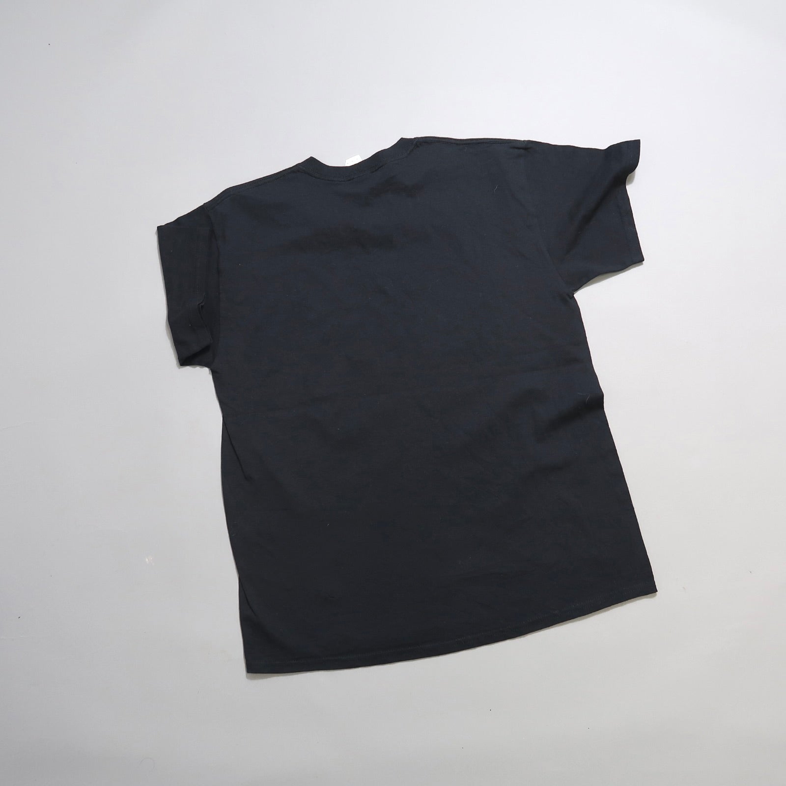 A plain black T-shirt laid flat on a light gray background.