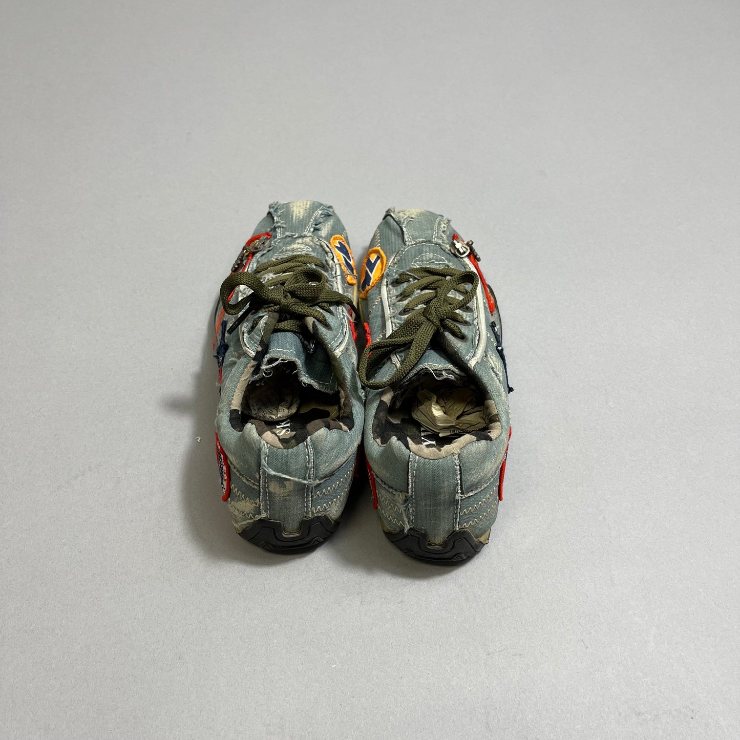 Worn-out sneakers with colorful patches on a gray surface.