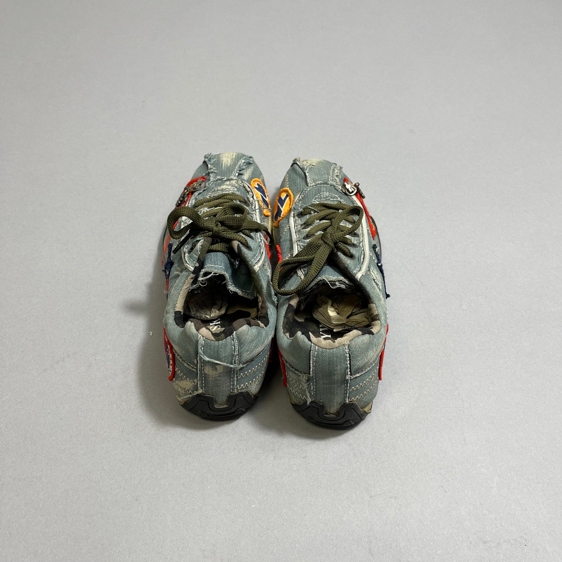 Worn-out sneakers with colorful patches on a gray surface.