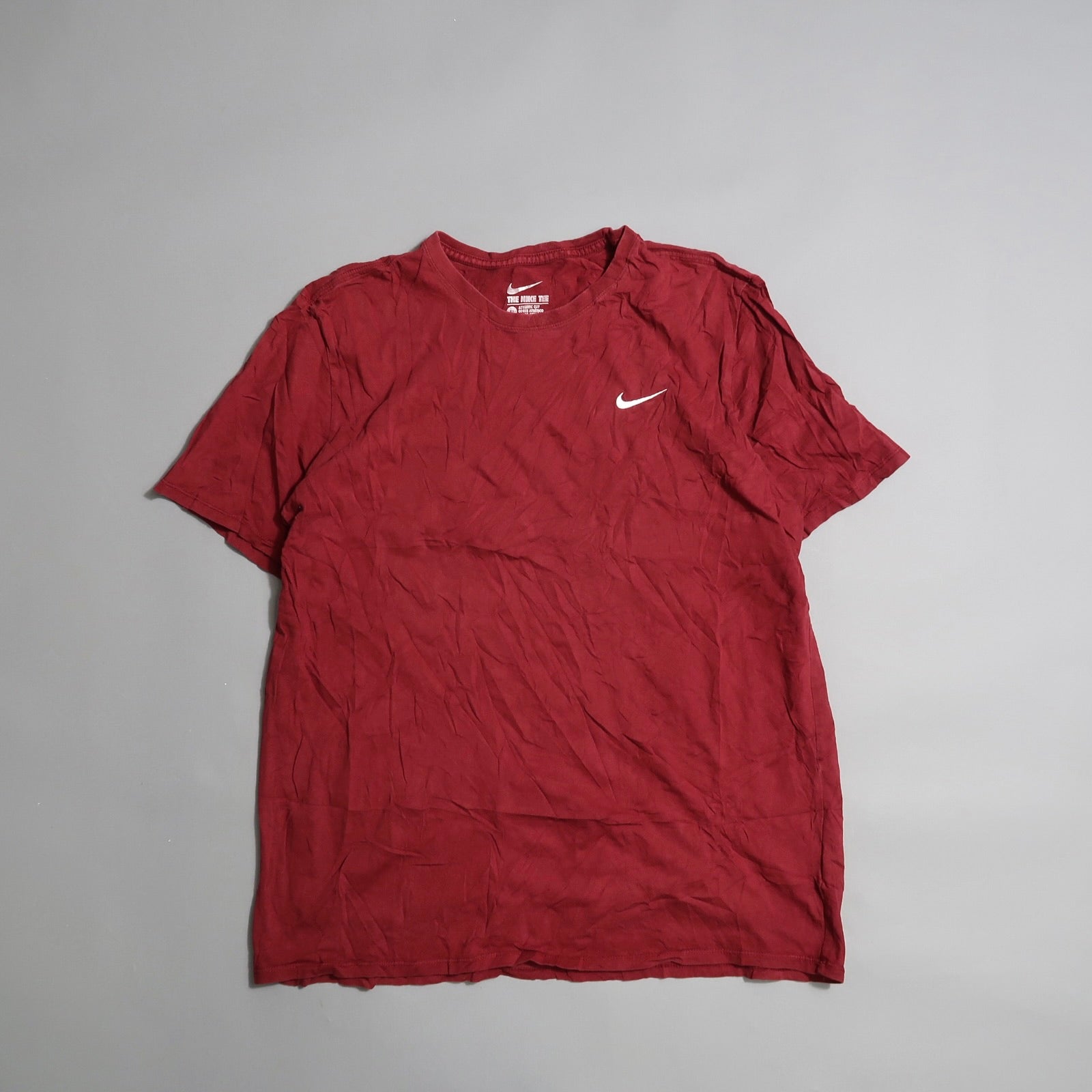 Wrinkled red T-shirt with a white swoosh logo on a gray background.