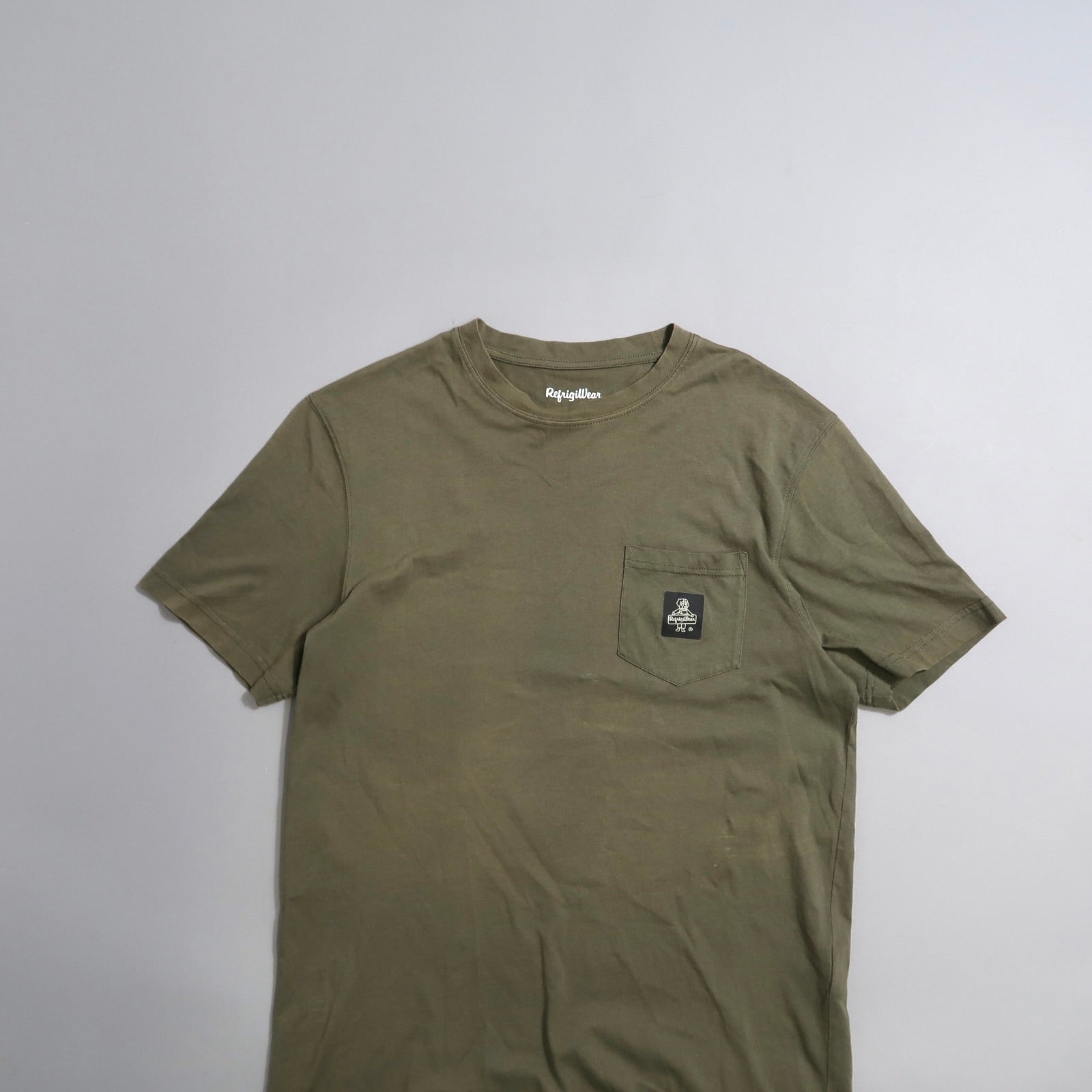 Olive green t-shirt with a chest pocket and logo patch.