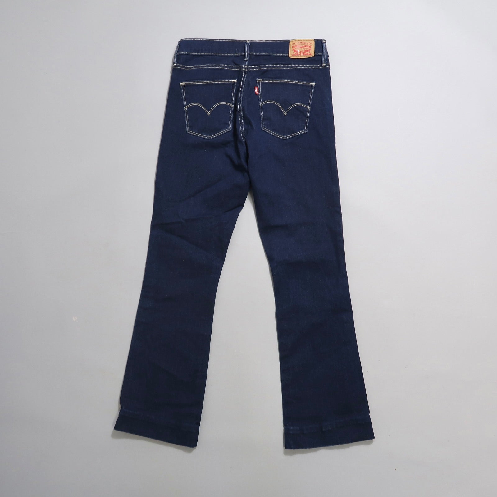 Dark blue jeans with back pockets, displayed flat on a light surface.