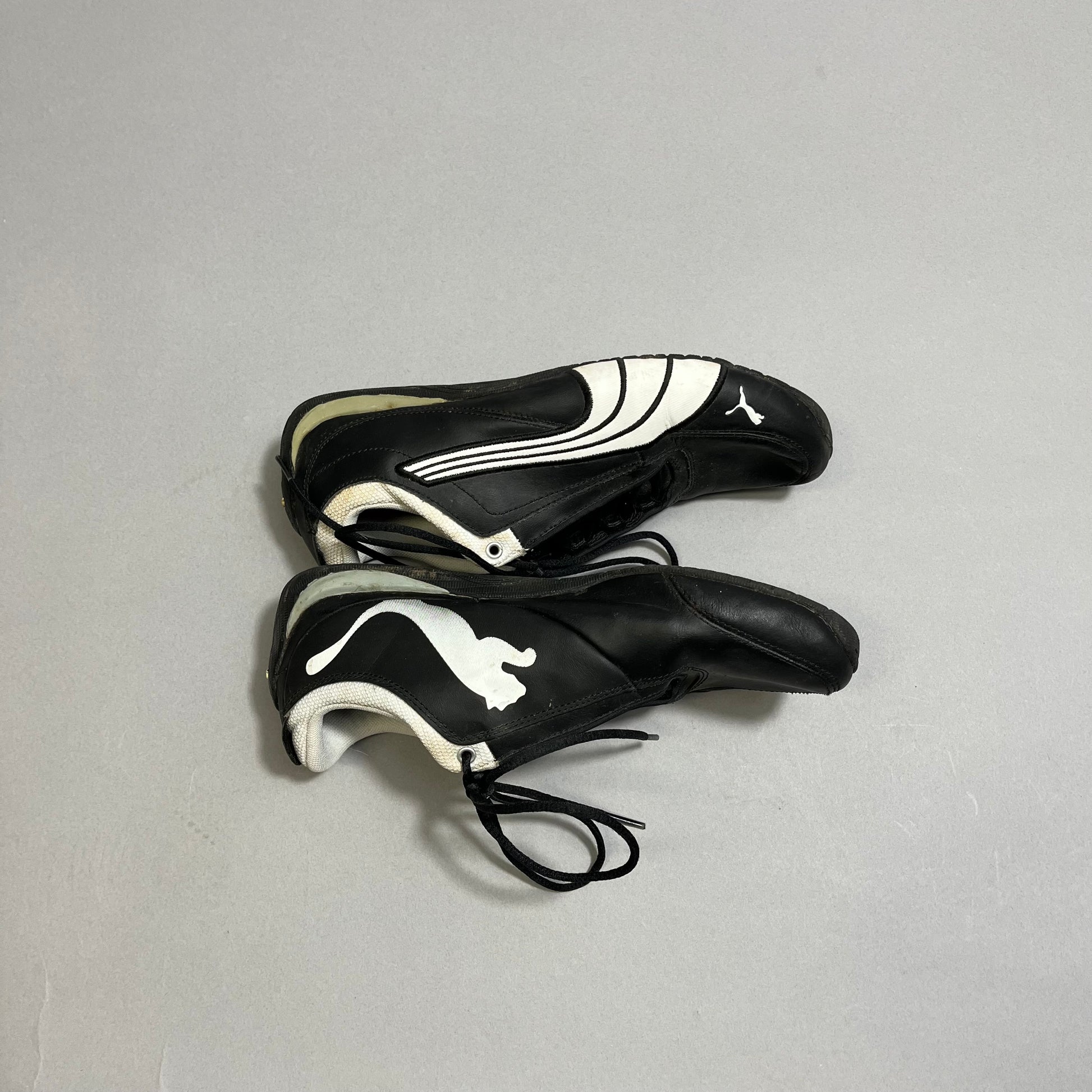 Black racing shoes with white logo and design, laces untied.