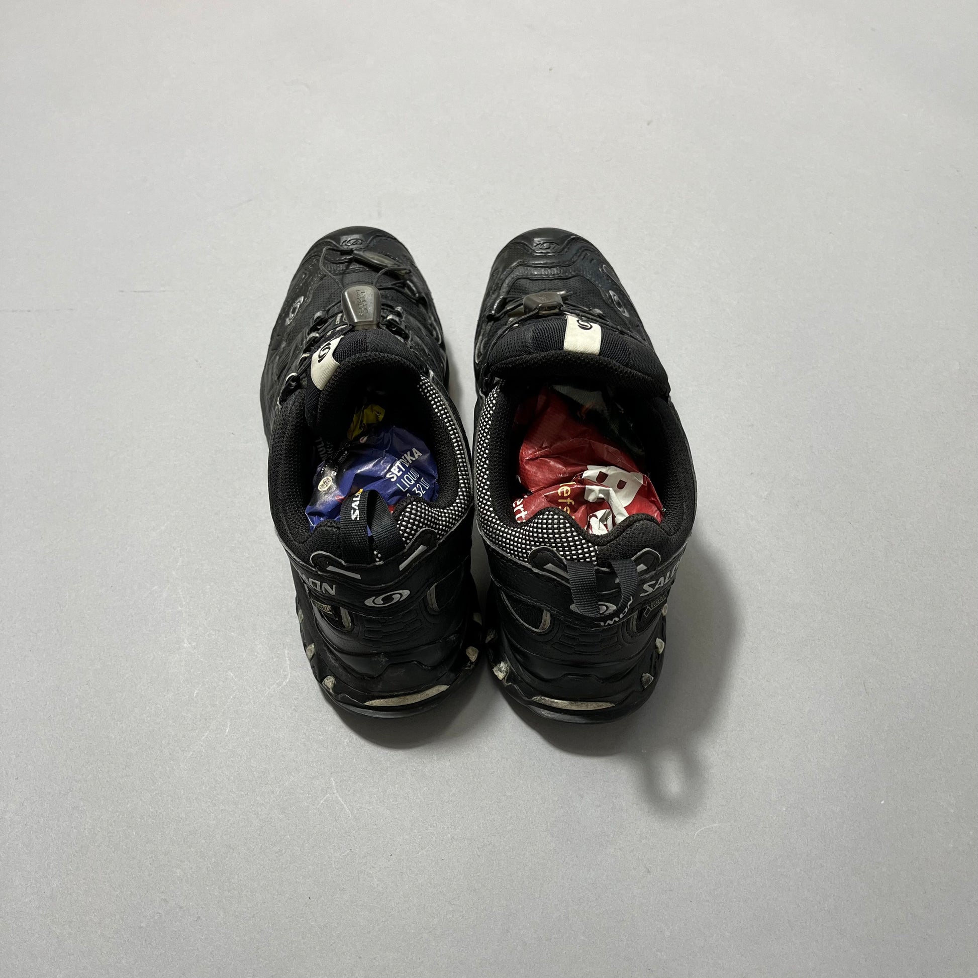 Black shoes stuffed with colorful crumpled paper on a gray surface.