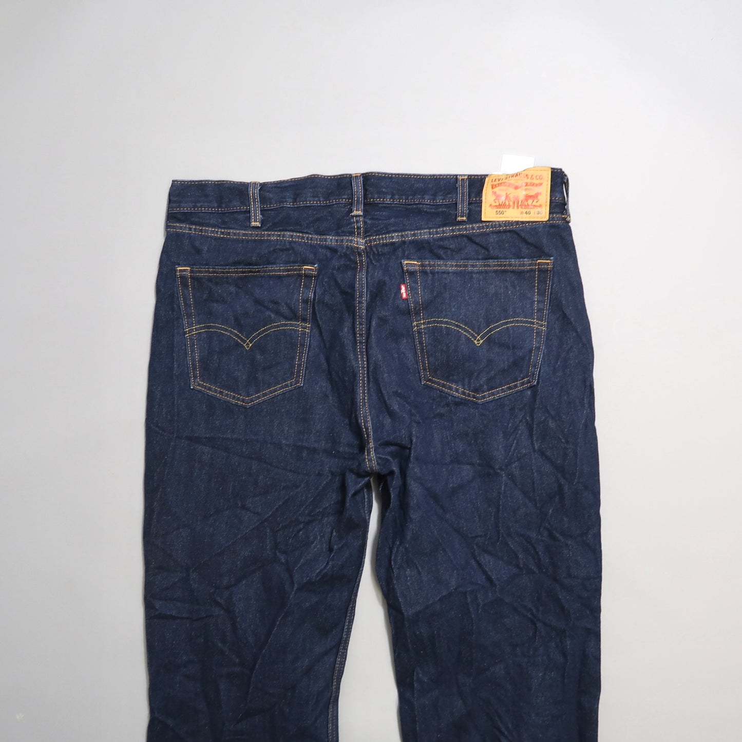 Back view of dark blue jeans with pockets and a leather label.