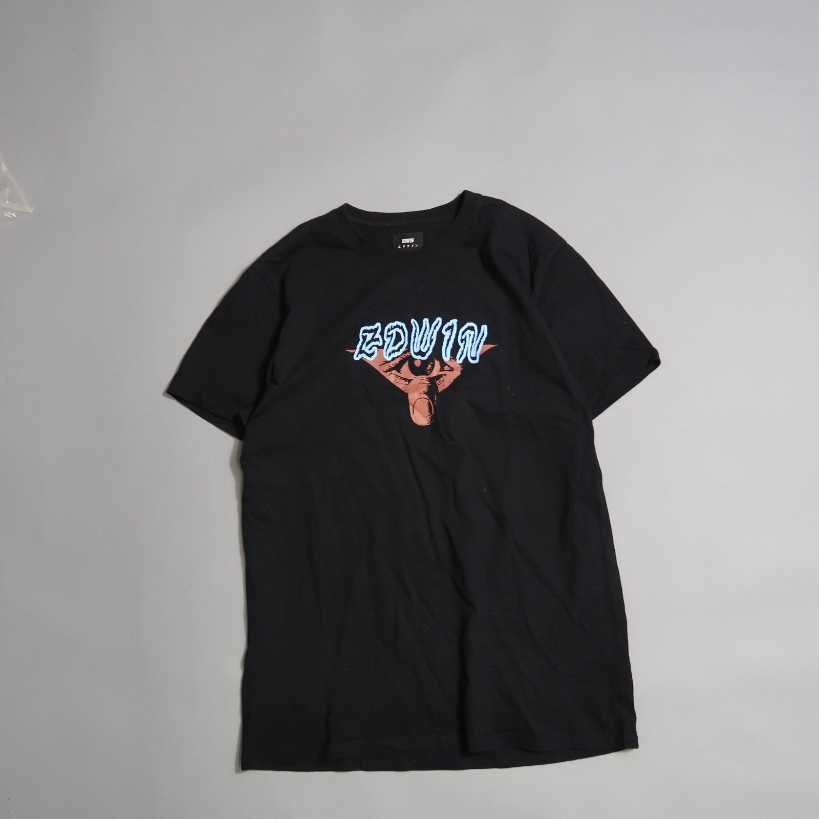 Black T-shirt with nullEDWINnull and artwork on the front, laid on gray surface.