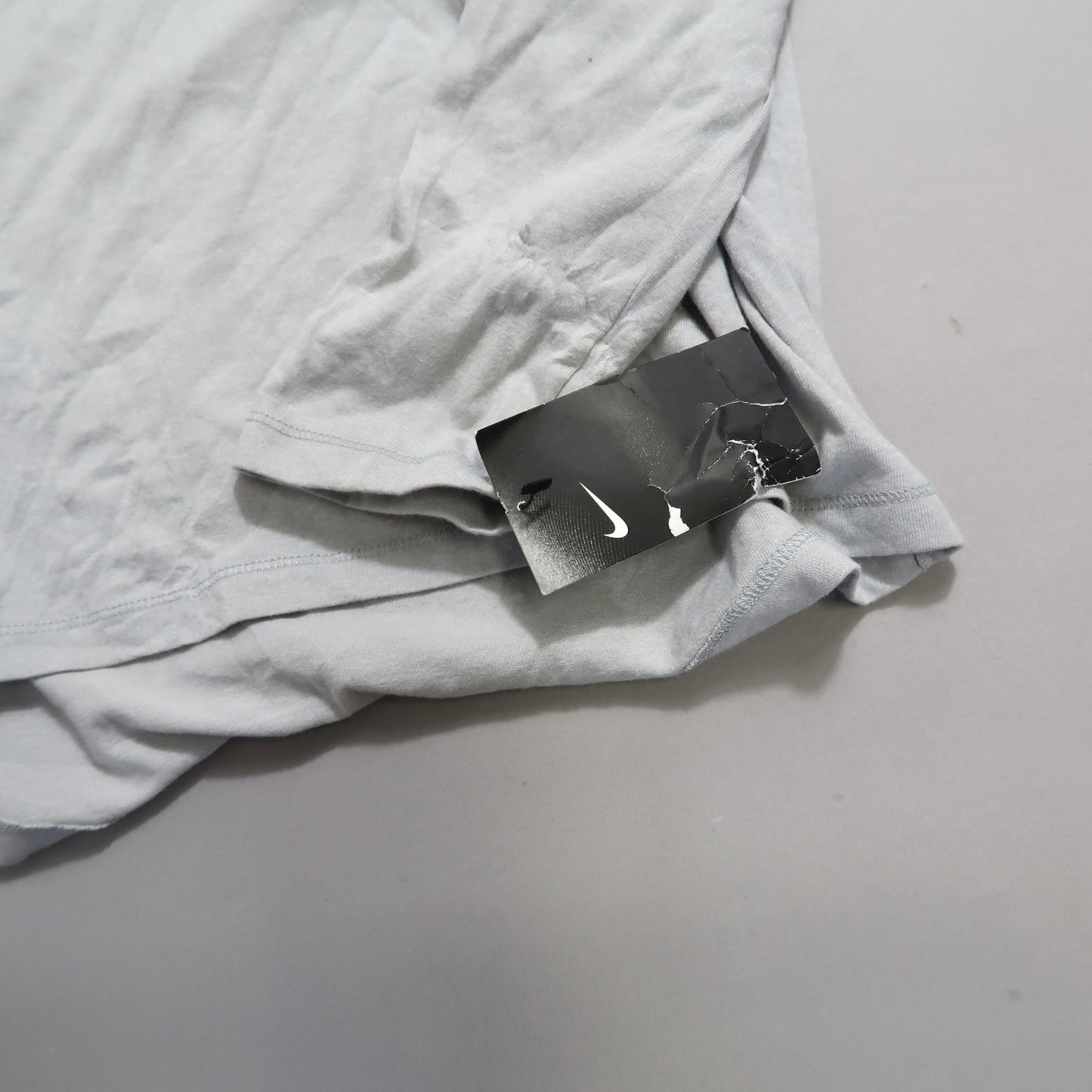 Gray T-shirt with a crumpled Nike tag on a light background.