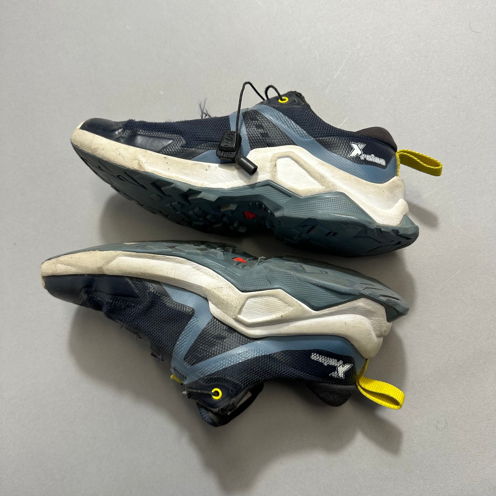 Blue and gray trail running shoes with rugged soles on a gray background.