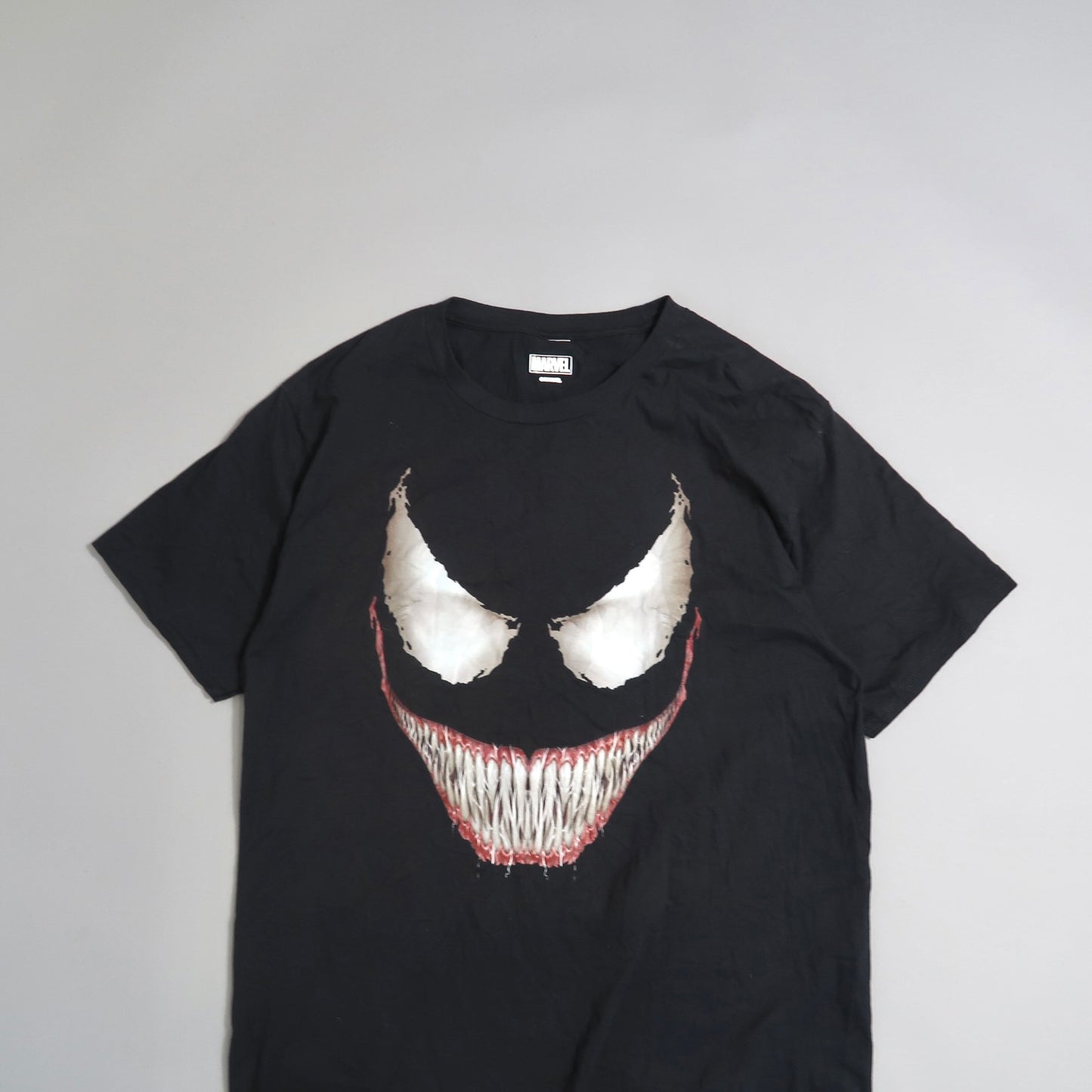 Black t-shirt with a stylized white grin and red eyes graphic design.