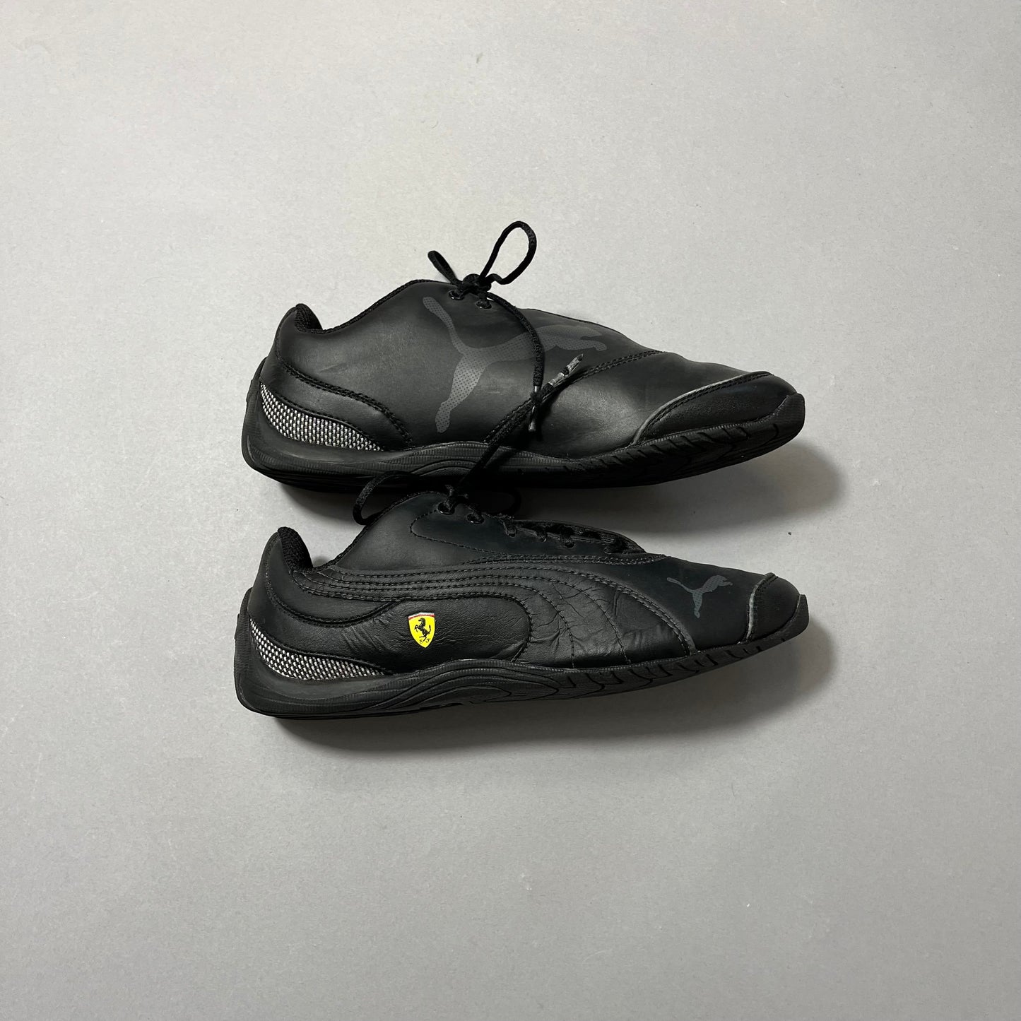 Black athletic shoes with Puma and Ferrari logos on gray background.