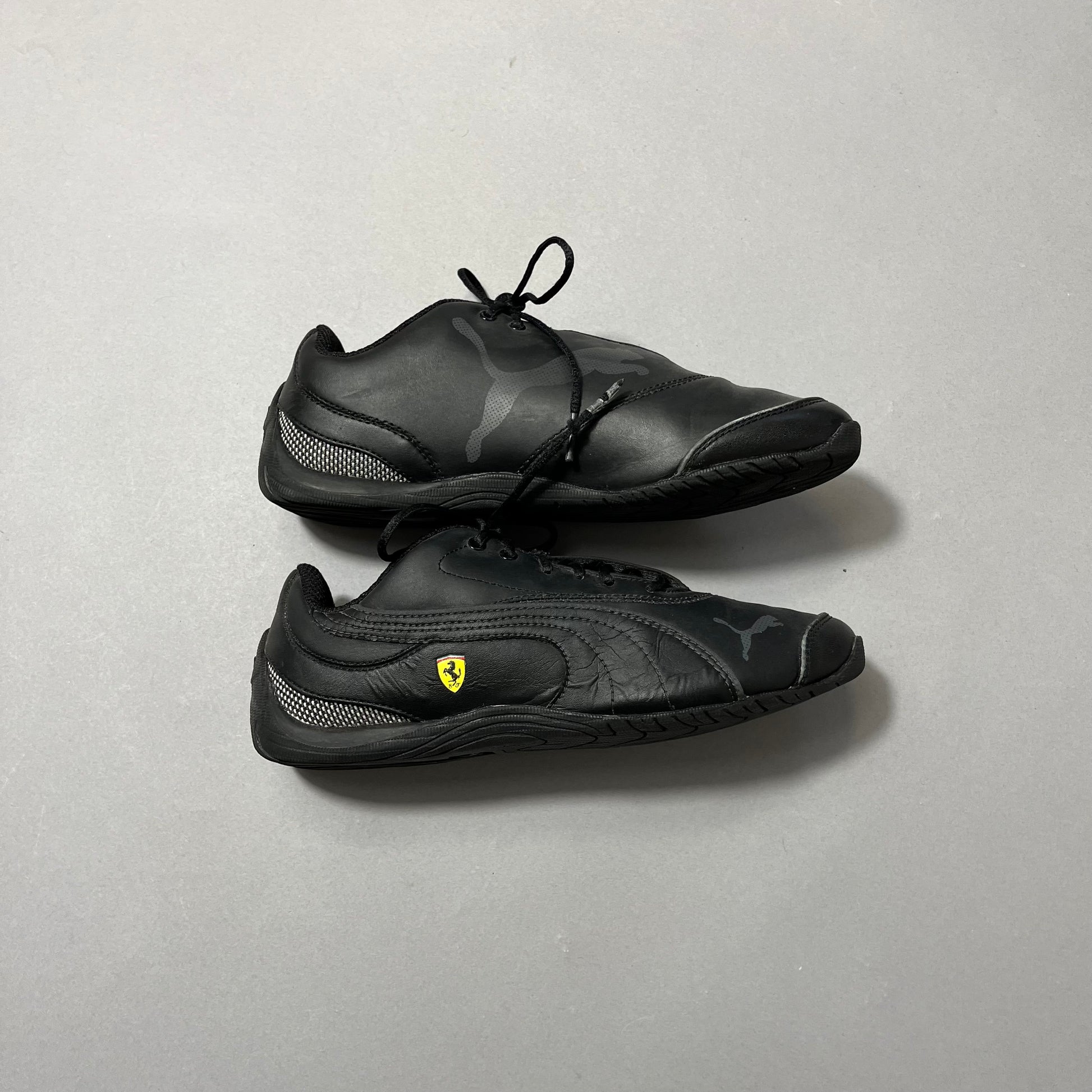 Black athletic shoes with Puma and Ferrari logos on gray background.