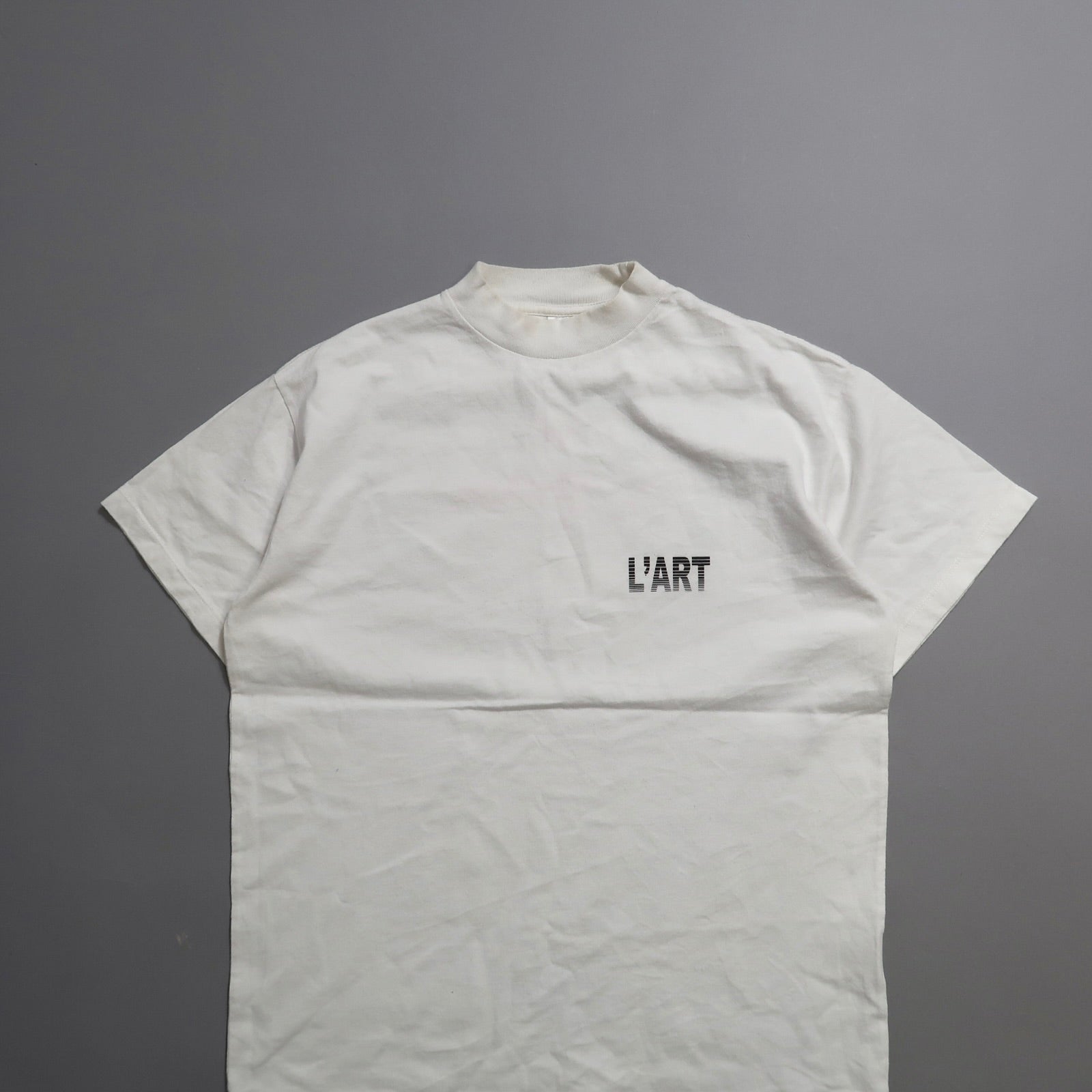 White T-shirt with nullL'ARTnull text on a gray background.