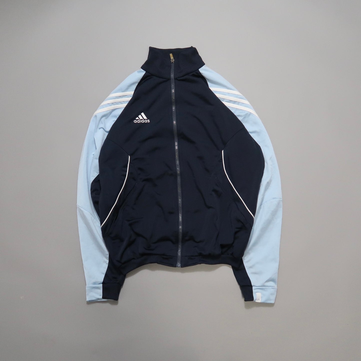 Navy and light blue Adidas track jacket on gray background.