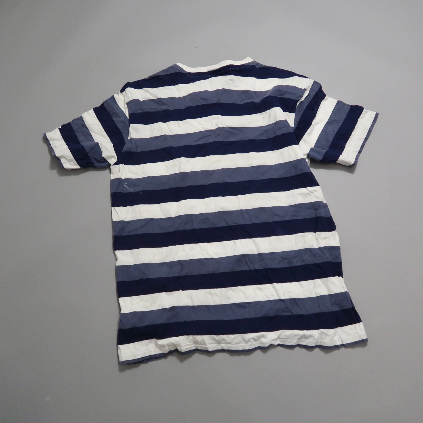 Blue and white striped T-shirt laid flat on a gray surface.