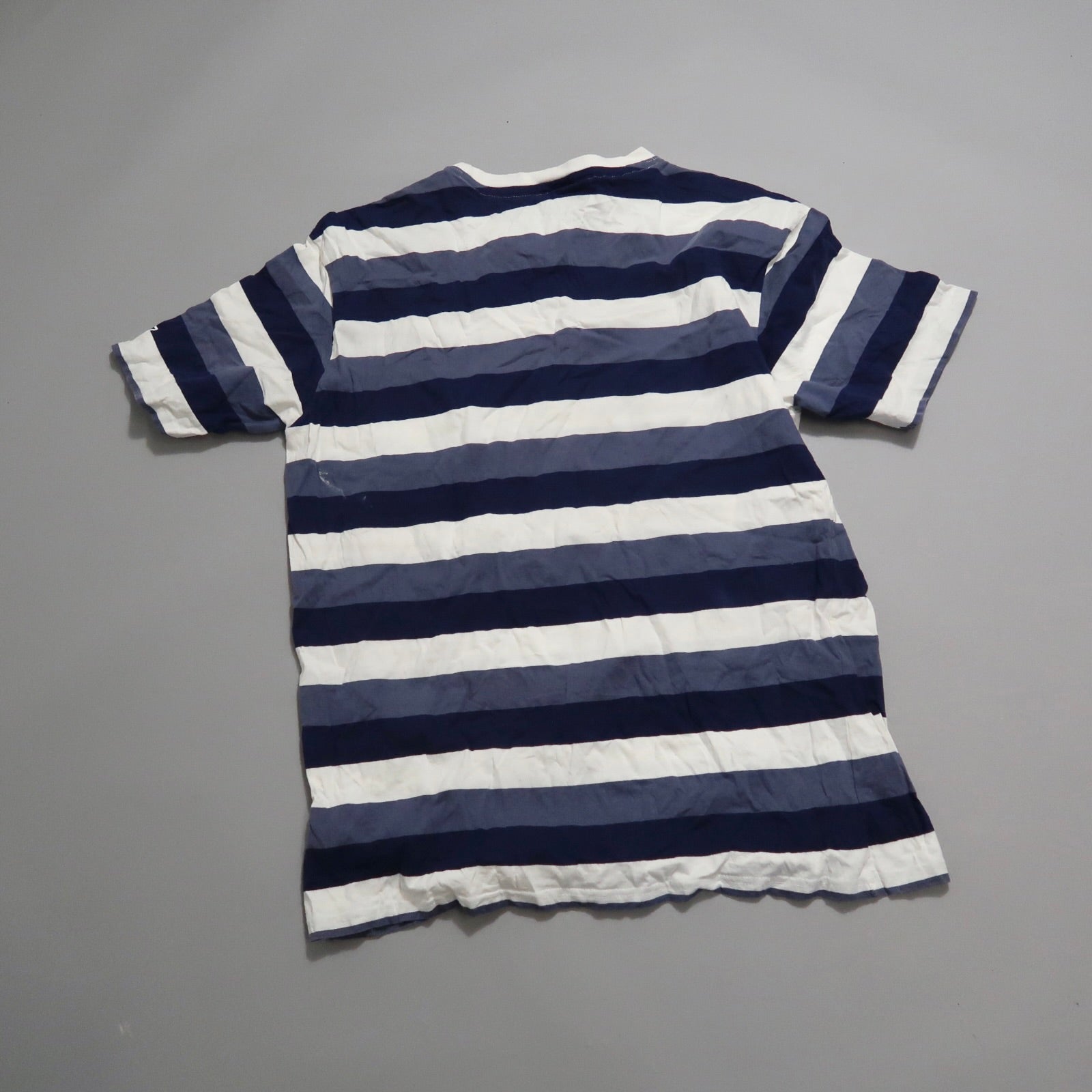 Blue and white striped T-shirt laid flat on a gray surface.