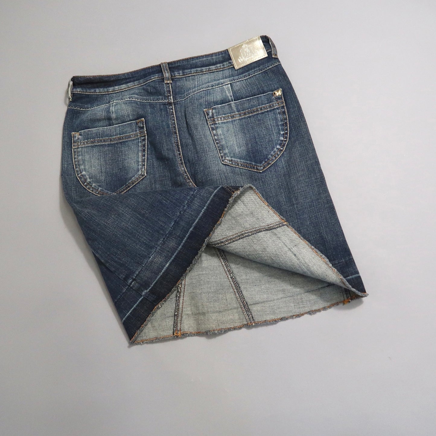 Denim skirt with a frayed hem on a gray background.