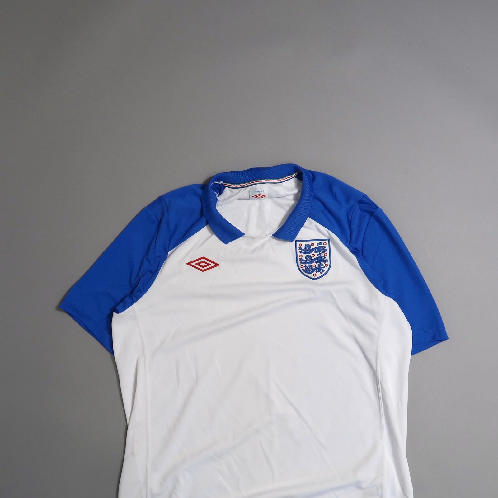 White and blue sports jersey with a crest and logo, on a gray background.