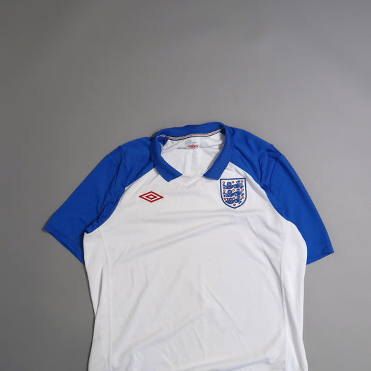 White and blue sports jersey with a crest and logo, on a gray background.