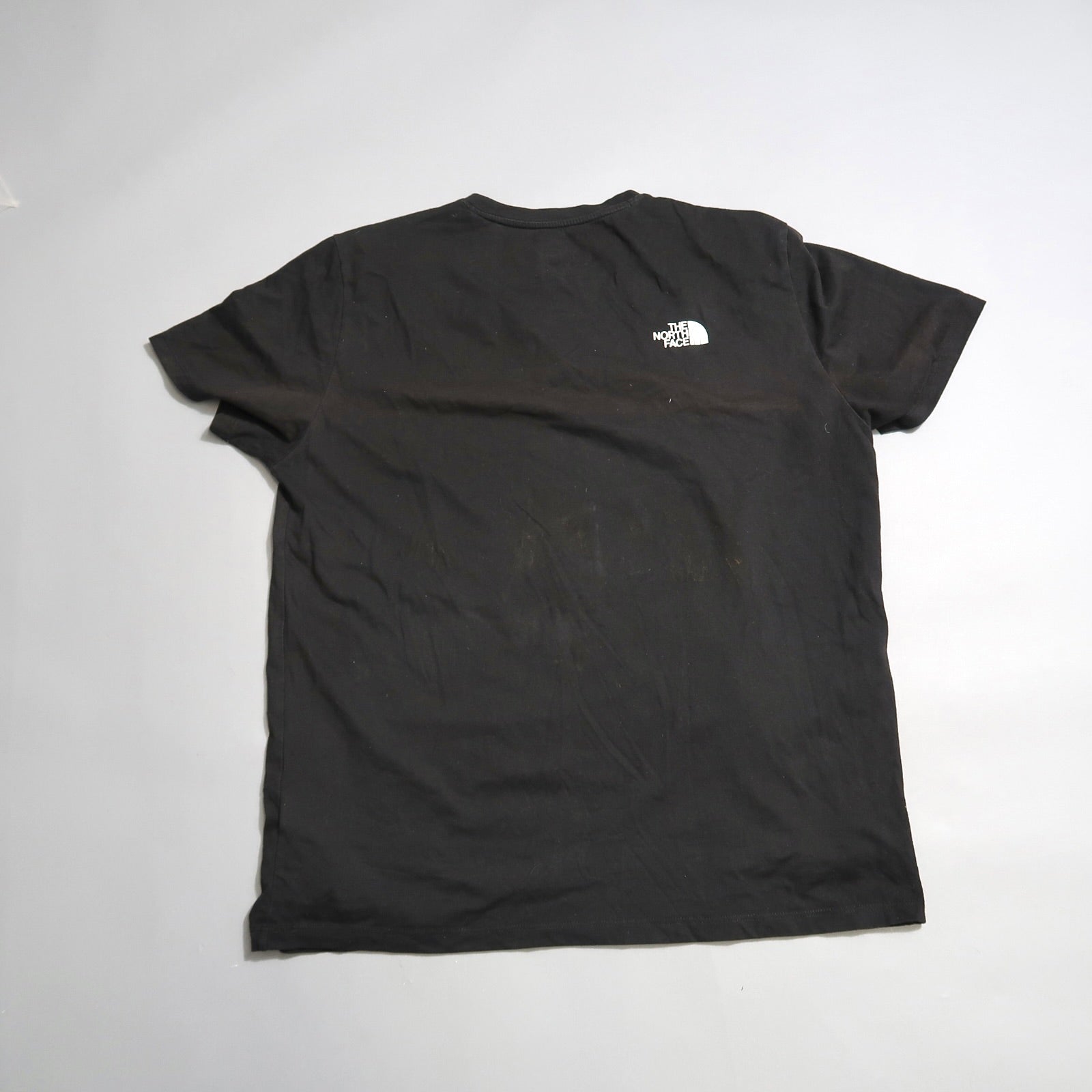 Black T-shirt with a small logo on the back, displayed on a flat surface.