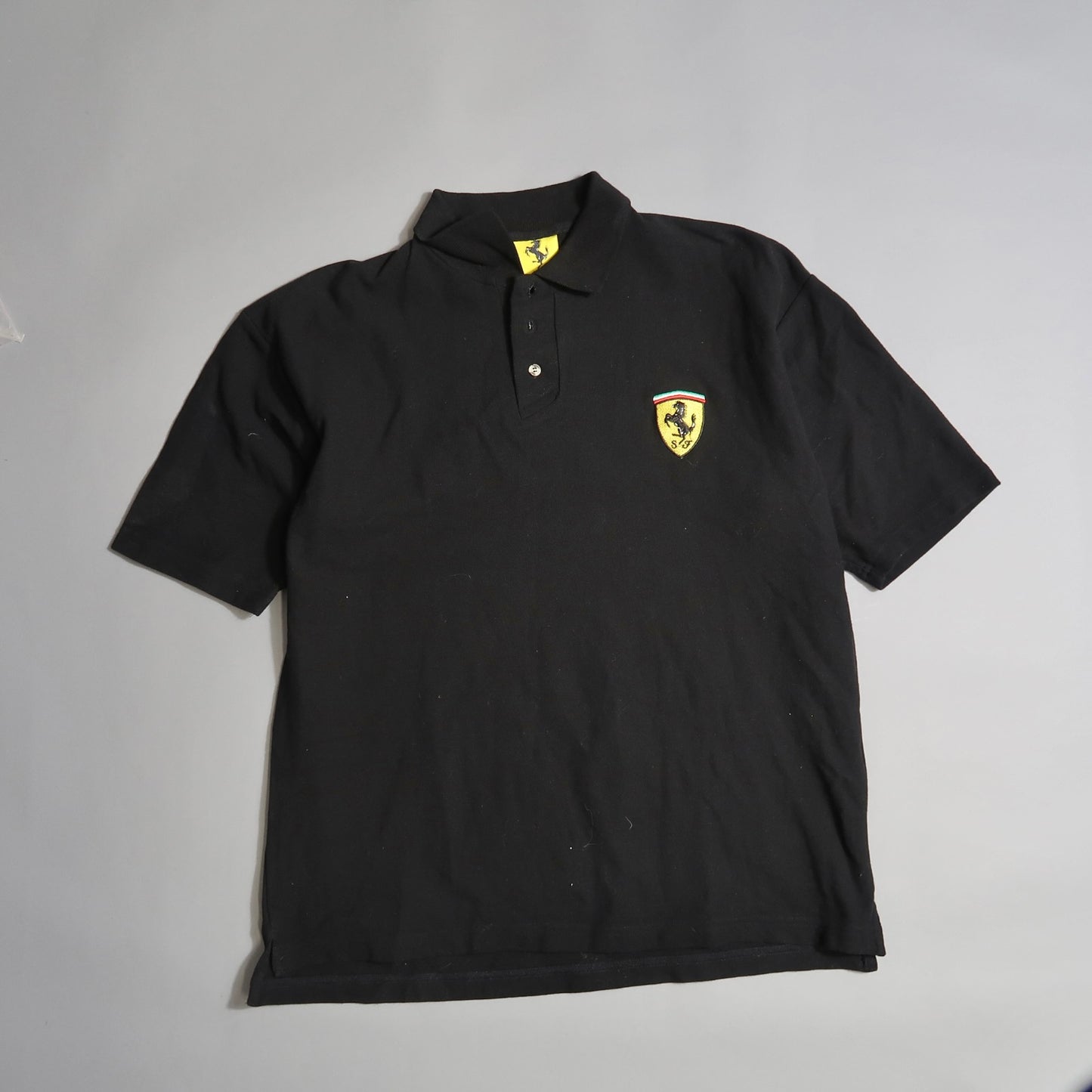 Black polo shirt with a yellow and black emblem on the chest.