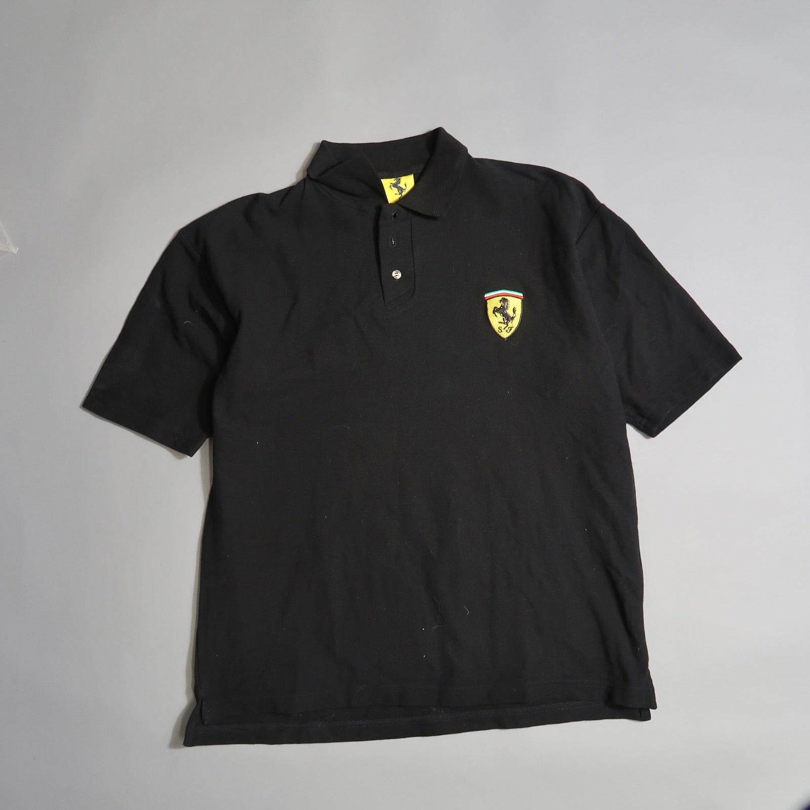 Black polo shirt with a yellow and black emblem on the chest.