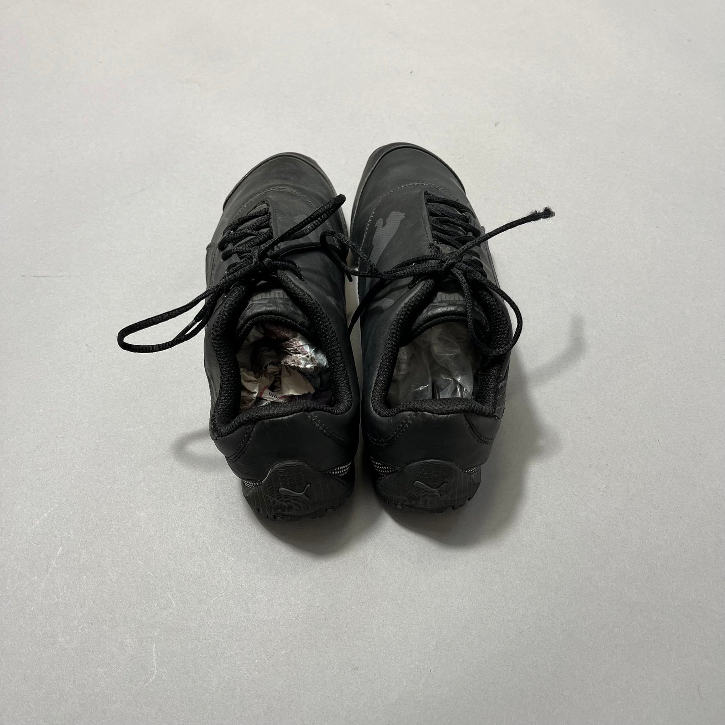 Black sneakers stuffed with paper, placed on a light surface.