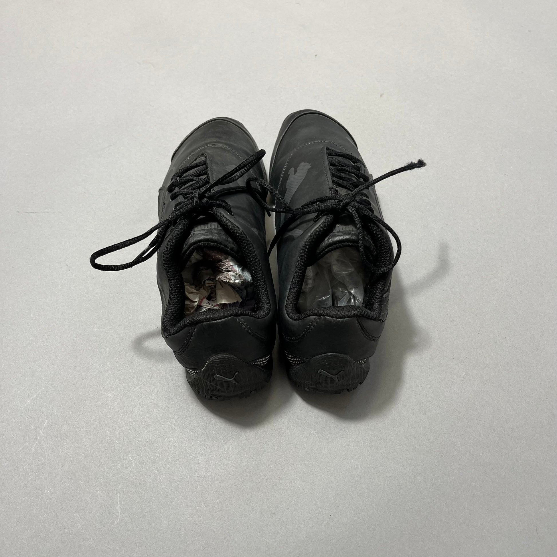 Black sneakers stuffed with paper, placed on a light surface.