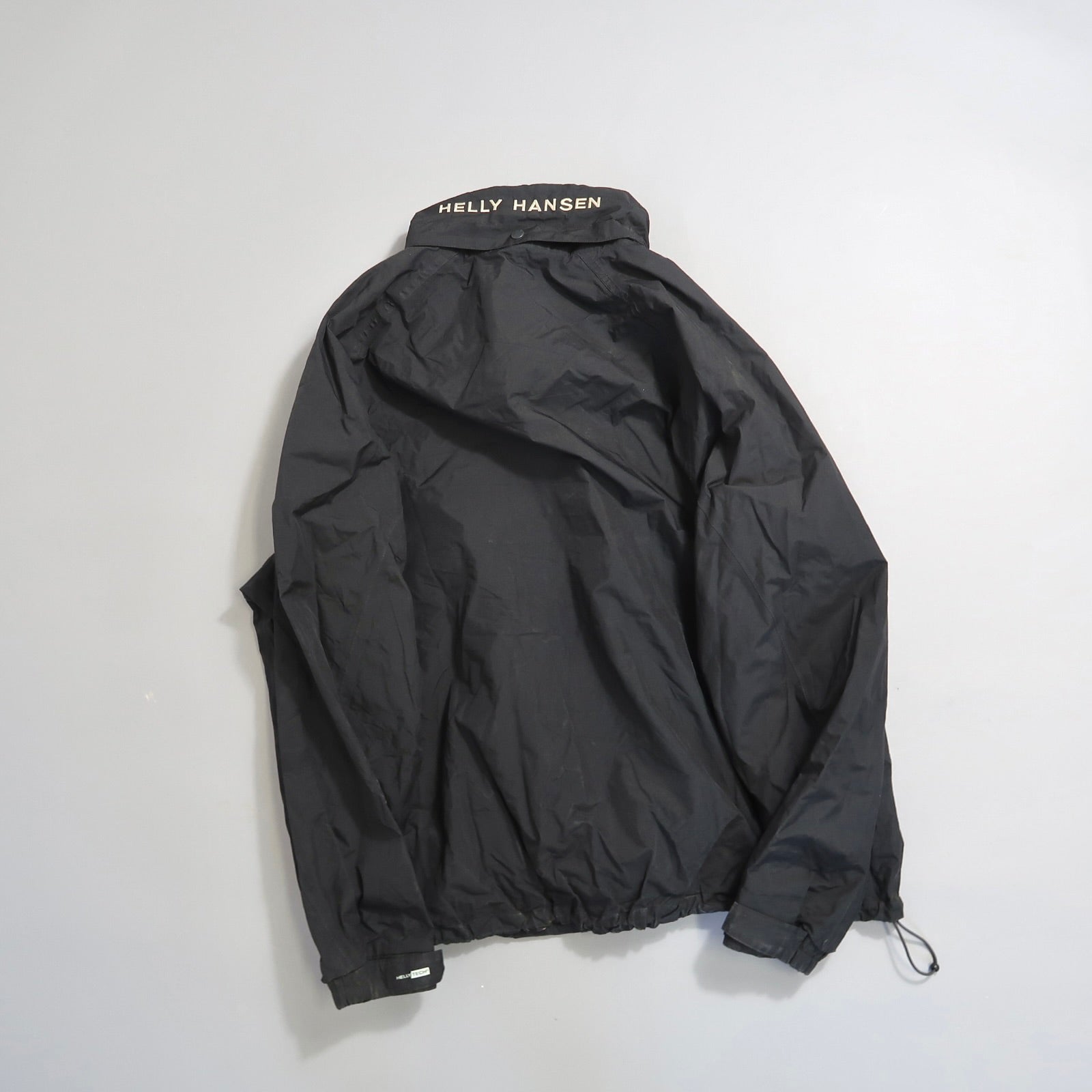 Black Helly Hansen jacket laid flat, showing back with logo collar.