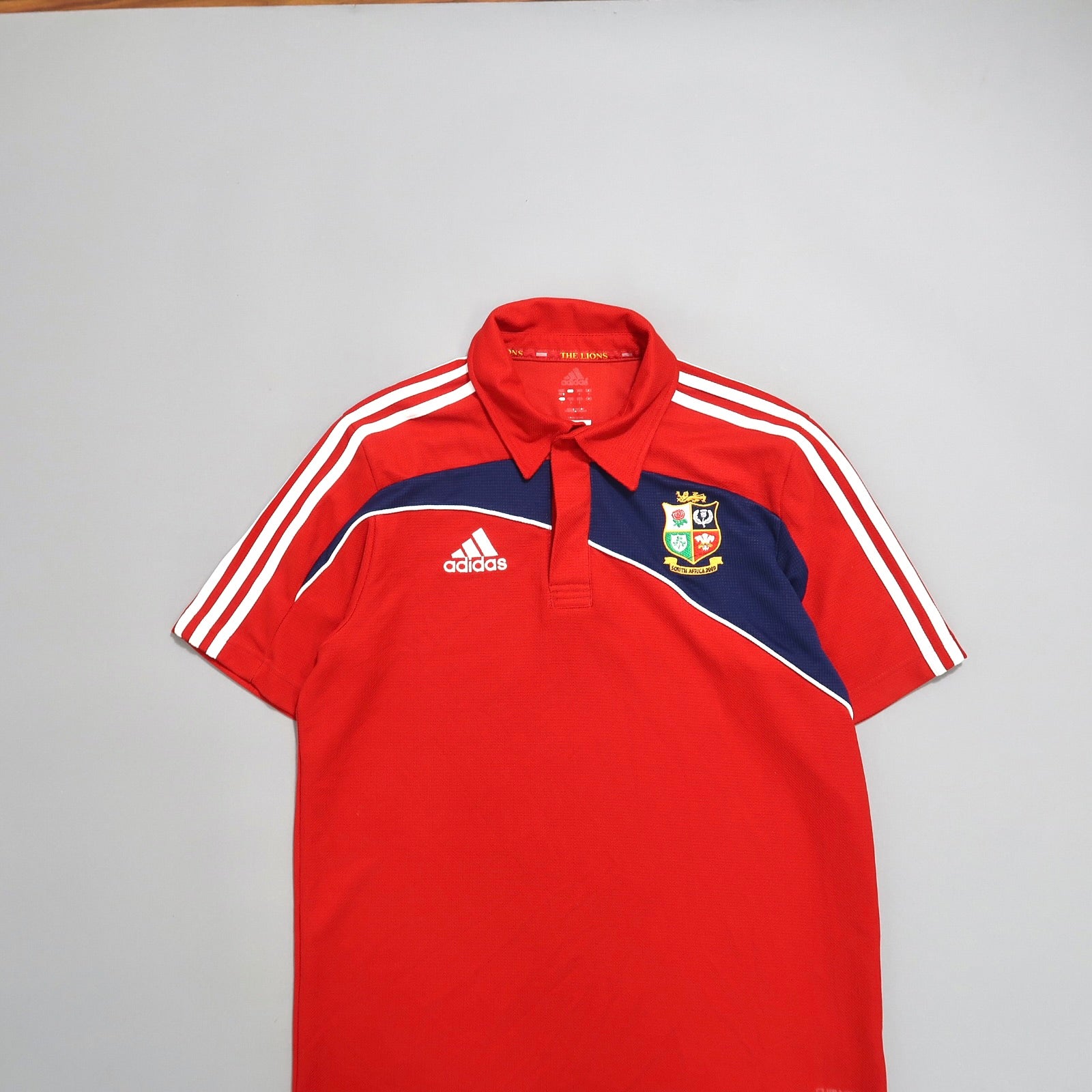 Red Adidas sports polo with a crest and white stripe accents.