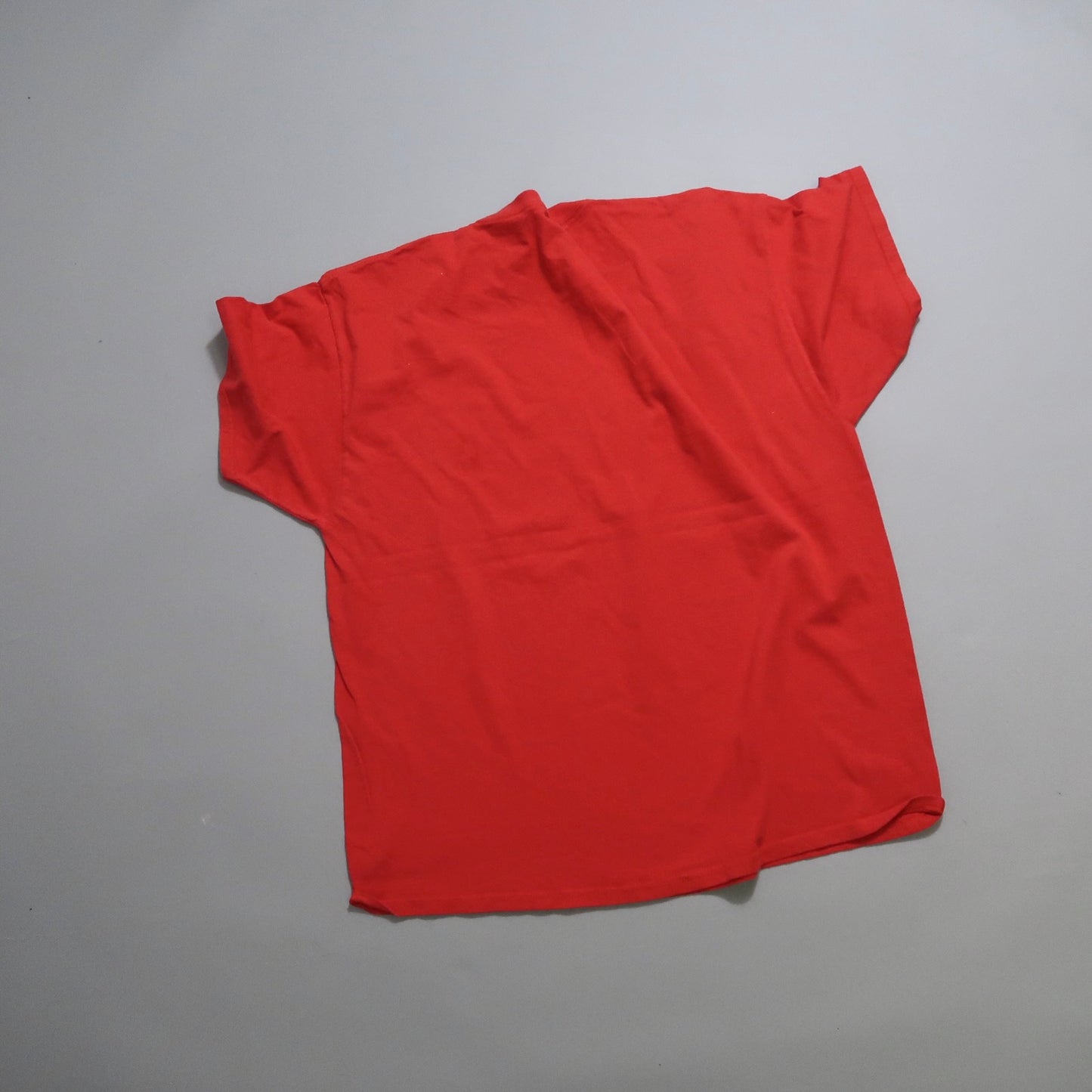Red T-shirt laid flat on a smooth gray surface.