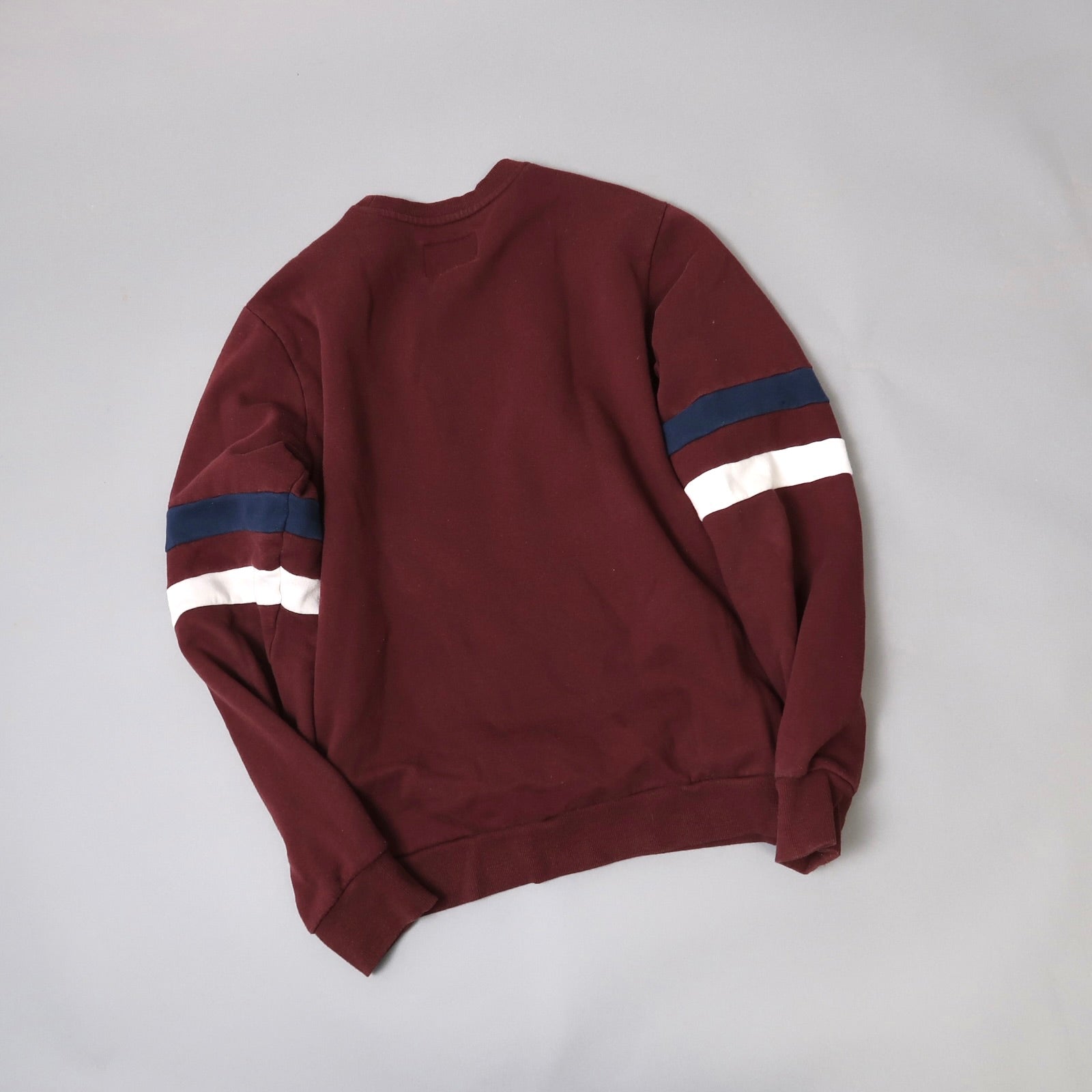 Maroon sweatshirt with blue and white striped sleeves on gray background.