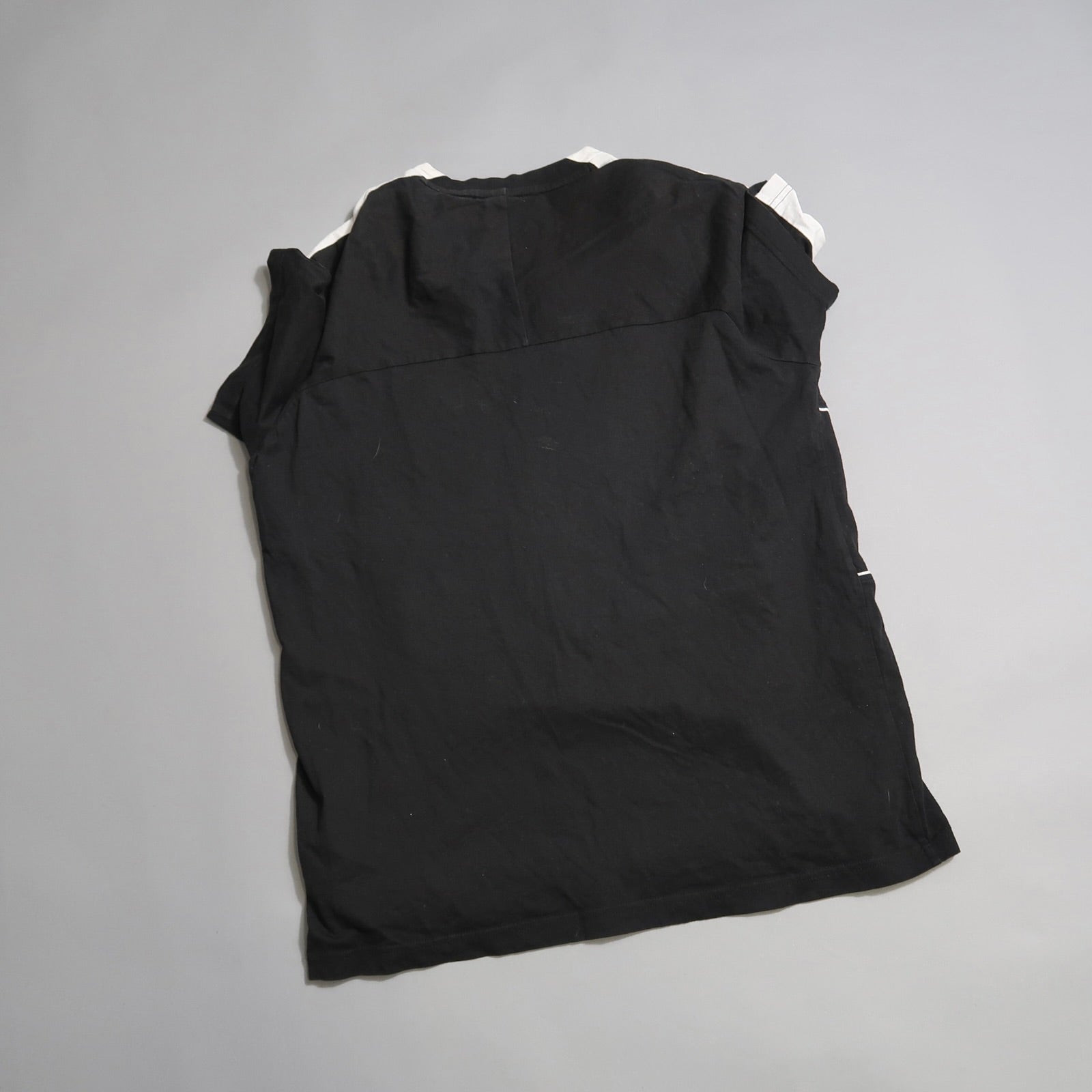 Black, sleeveless shirt laid flat on a light gray surface.