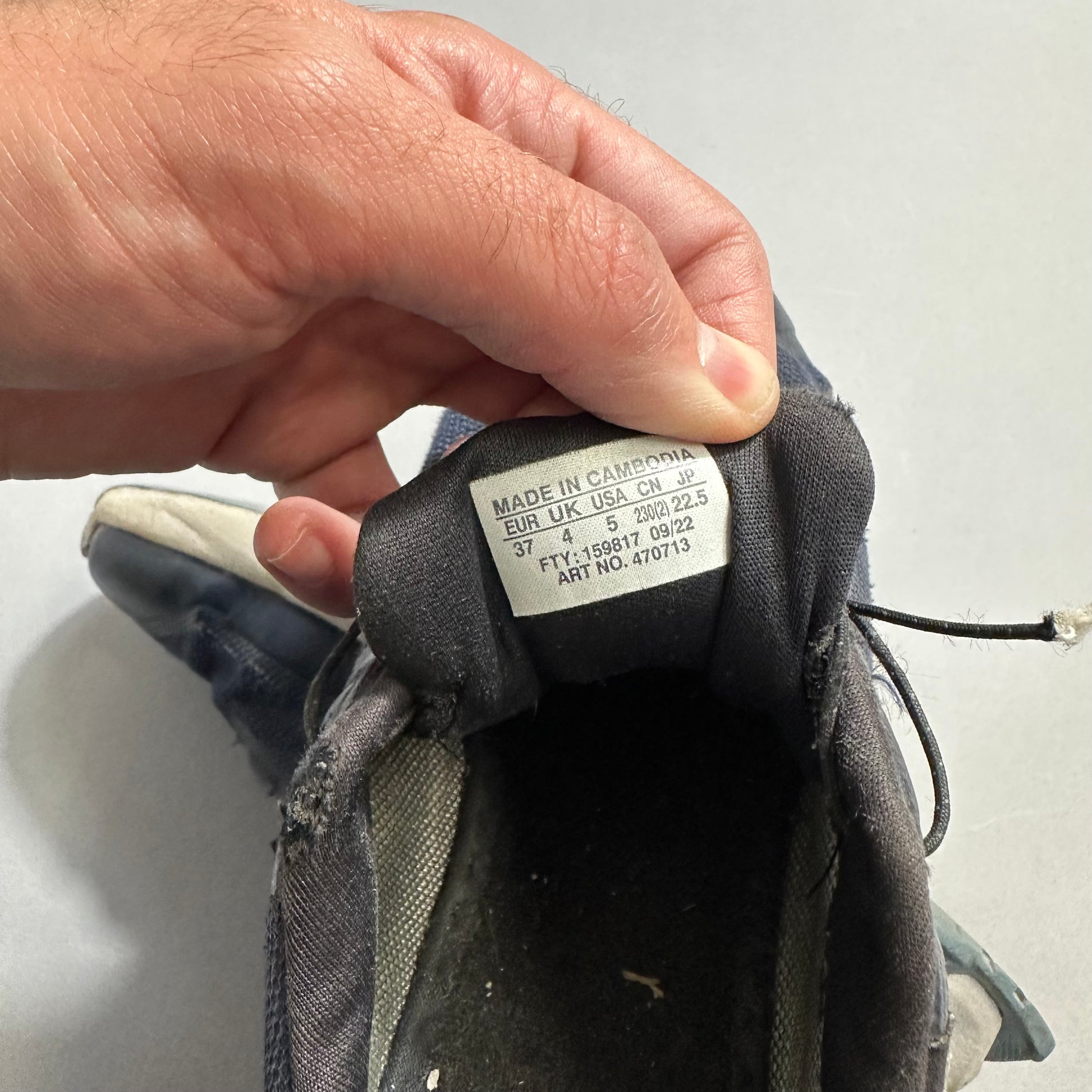 Hand holding a shoe with a nullMade in Cambodianull label showing sizes.