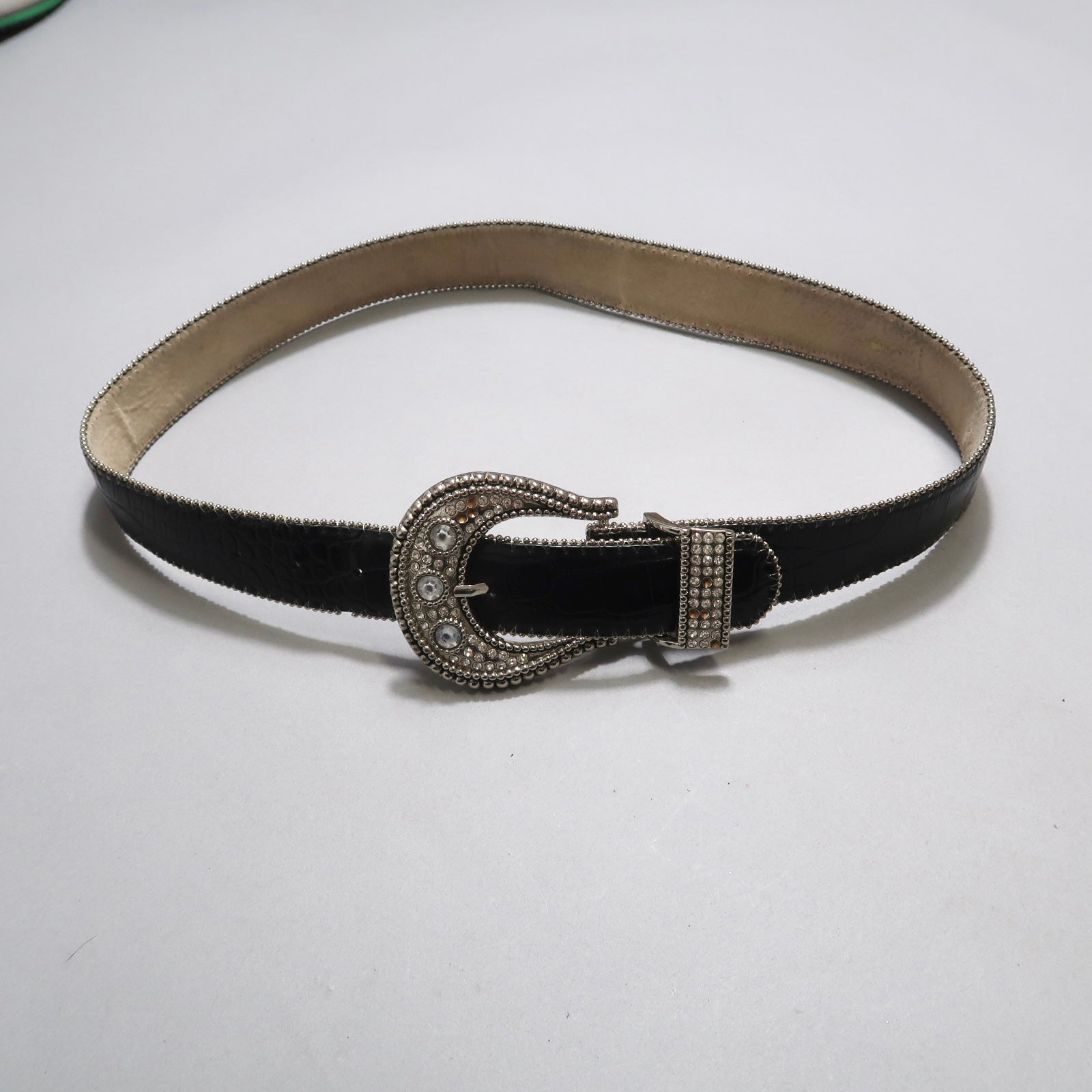 Black leather belt with an ornate silver buckle on a plain backdrop.