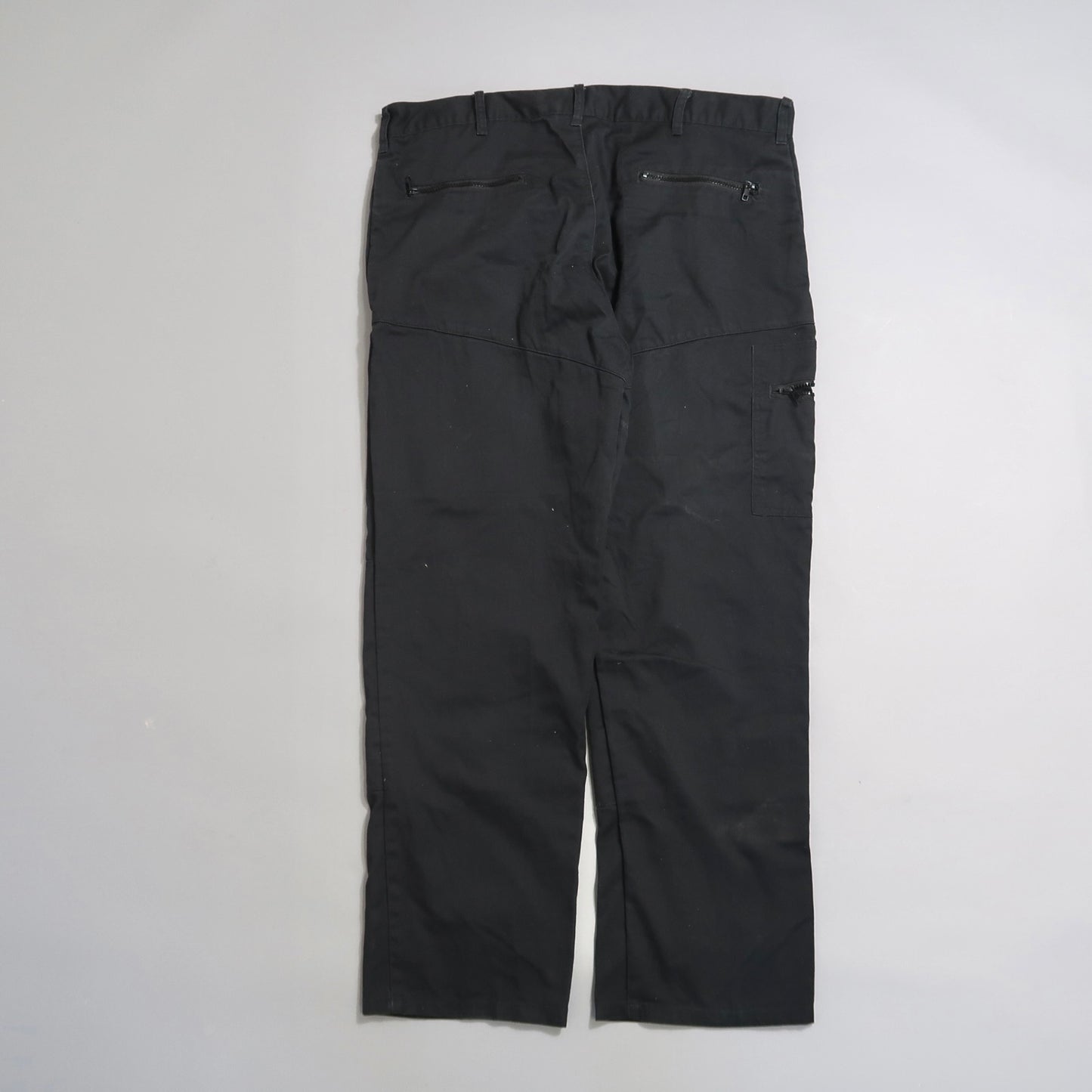 Black cargo pants with pockets and belt loops on a gray surface.