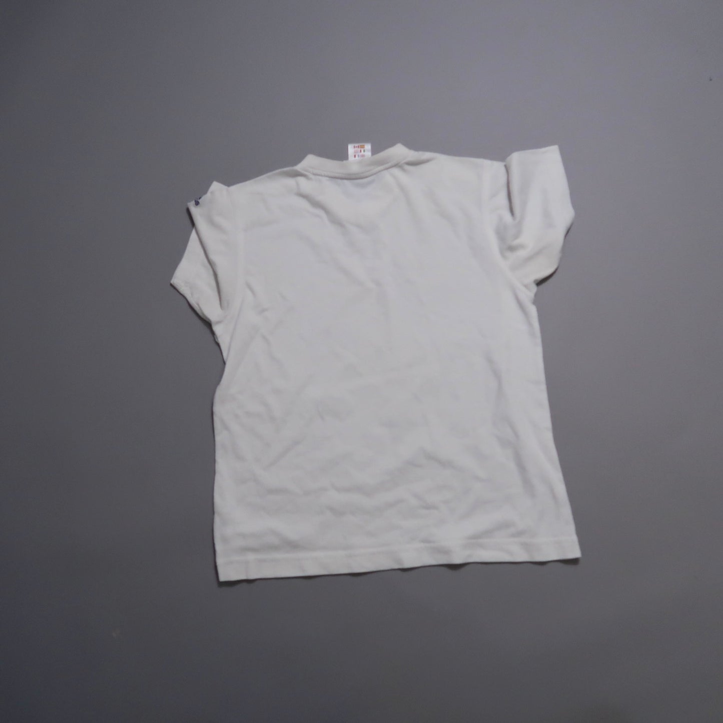 White T-shirt laid flat on a gray surface, viewed from the back.